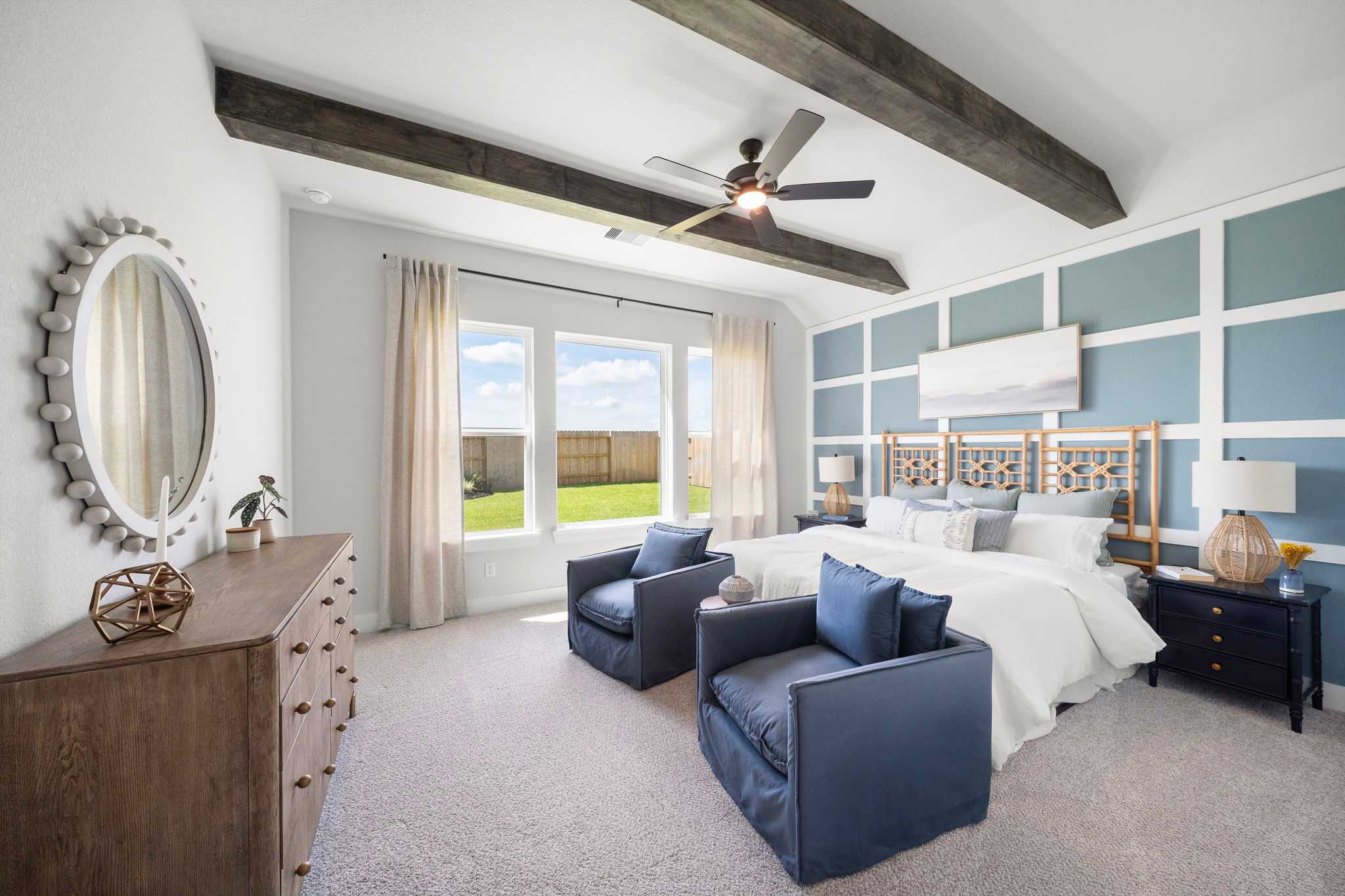 Spacious master bedroom at Lago Mar in Texas City TX with exposed beam ceiling, large windows overlooking yard, plush bed and blue armchairs