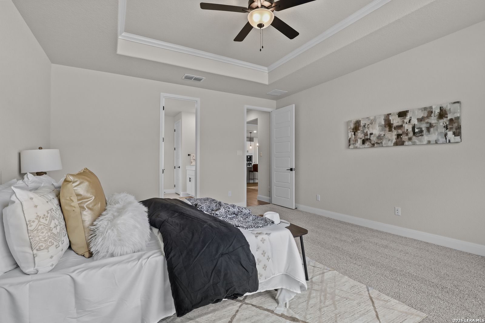 Elegant master bedroom with tray ceiling fan, king bed, decorative pillows and abstract art in Davidson Homes The Lanier G, Castroville, Texas