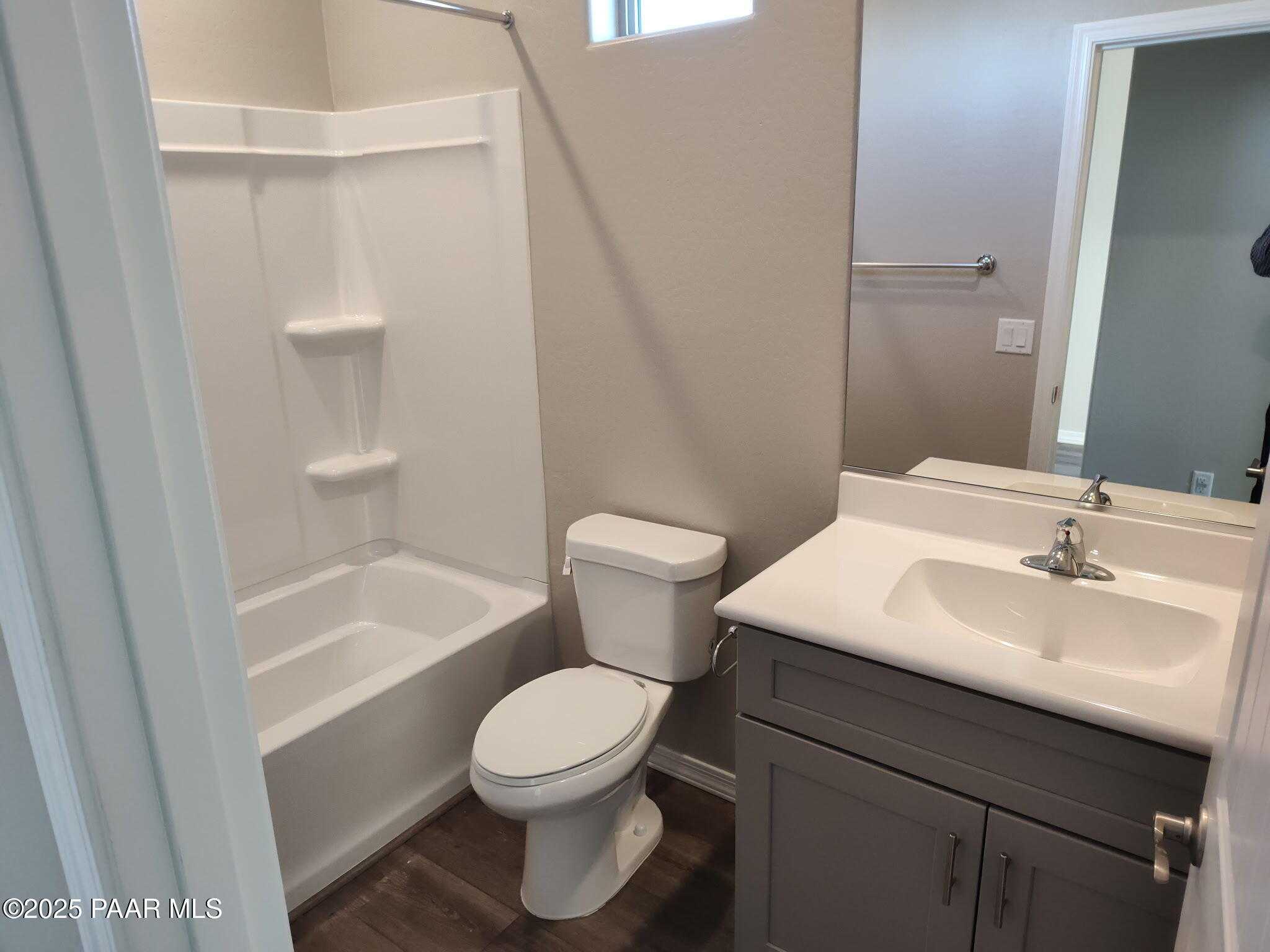 Modern bathroom with white tub-shower combo, grey vanity, toilet, and wood flooring in Davidson Homes The Frontier A, Prescott Valley, Arizona