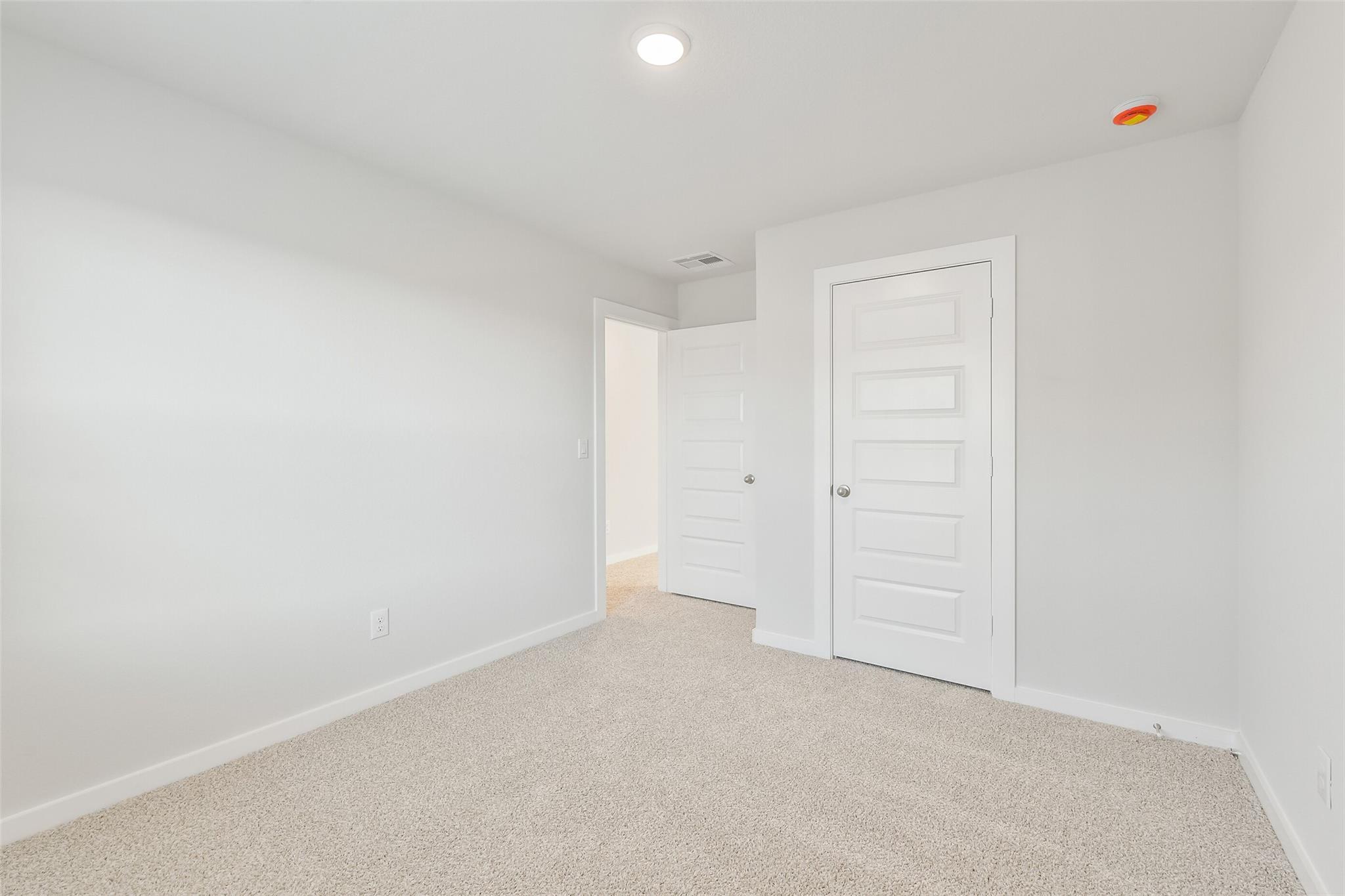 Bright secondary bedroom with white walls, beige carpet, and paneled doors in Davidson Homes The Trinity F, Magnolia, Texas