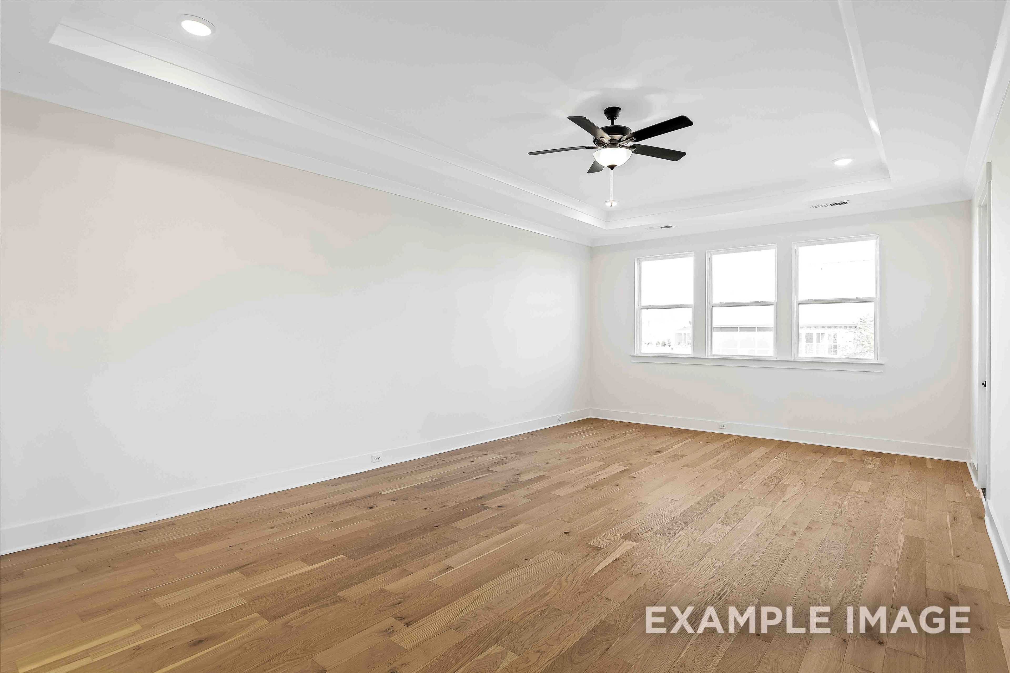 Spacious master bedroom in The Albany A featuring light oak hardwood floors, three large windows, white walls, and ceiling fan