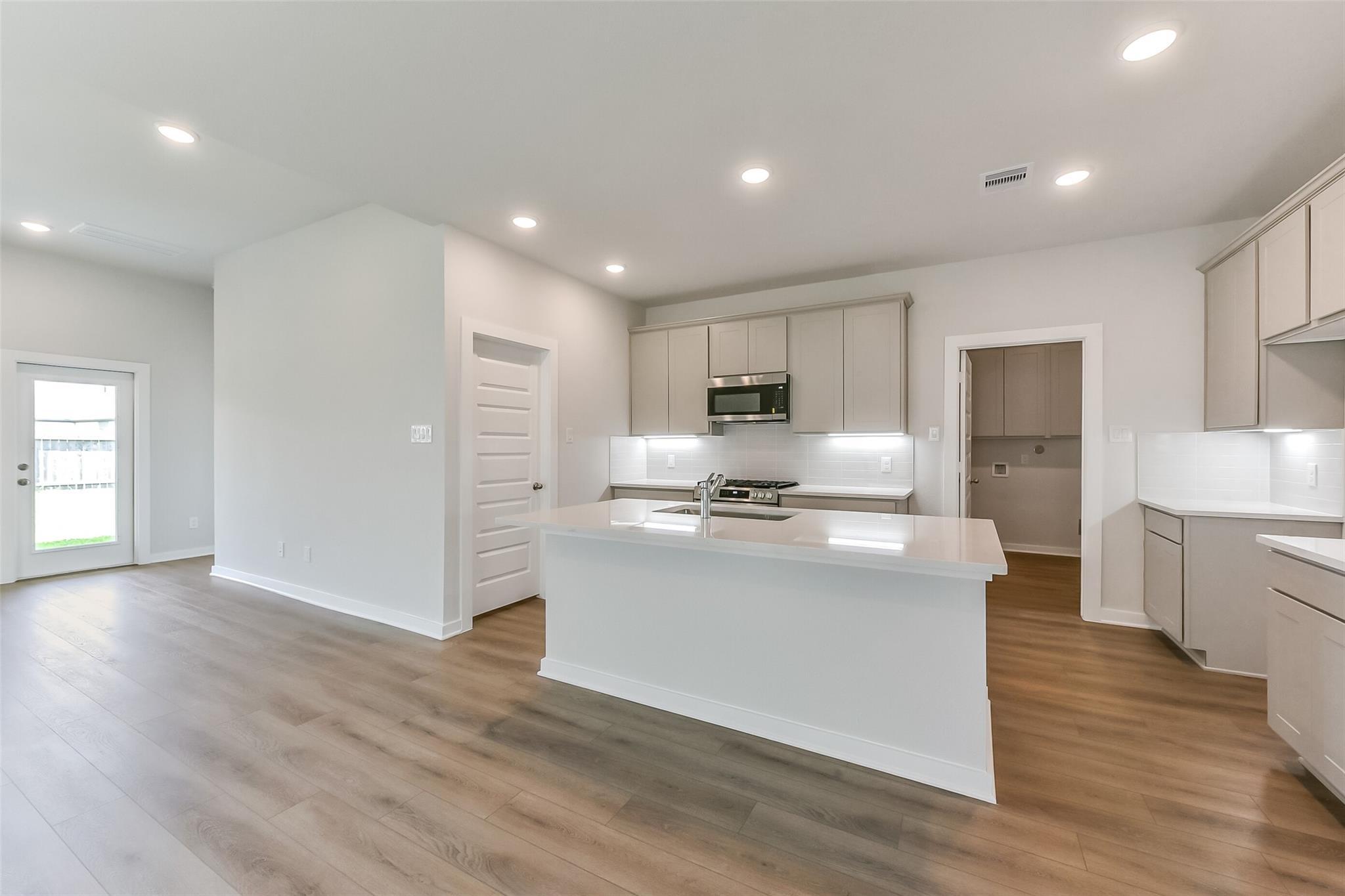 Modern open kitchen with white quartz island, shaker cabinets, stainless microwave in Davidson Homes The Tierra C, Dayton Texas