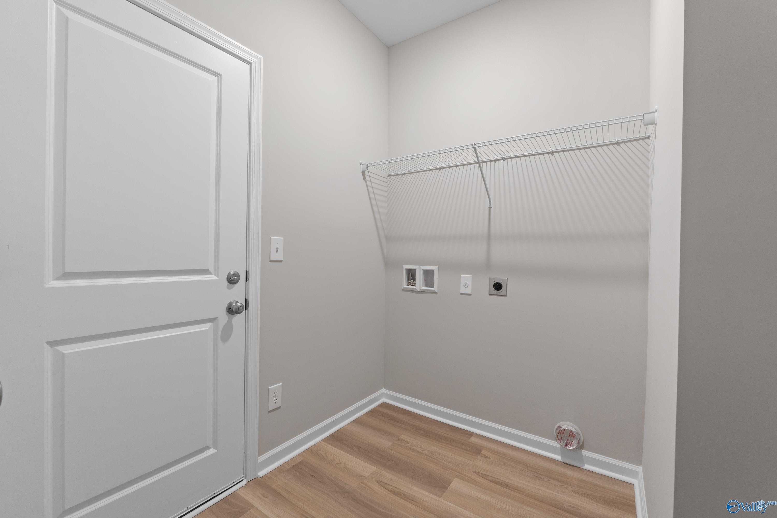 Spacious laundry room with washer dryer hookups, storage rod, and gray walls in Evermore Homes The Augusta, Madison Alabama