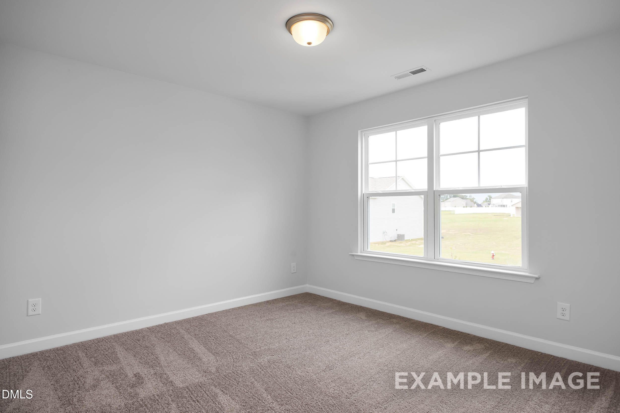Bright bedroom with neutral gray walls, beige carpet, flush-mount ceiling light, and large windows in Davidson Homes The Ash B, Lillington, NC