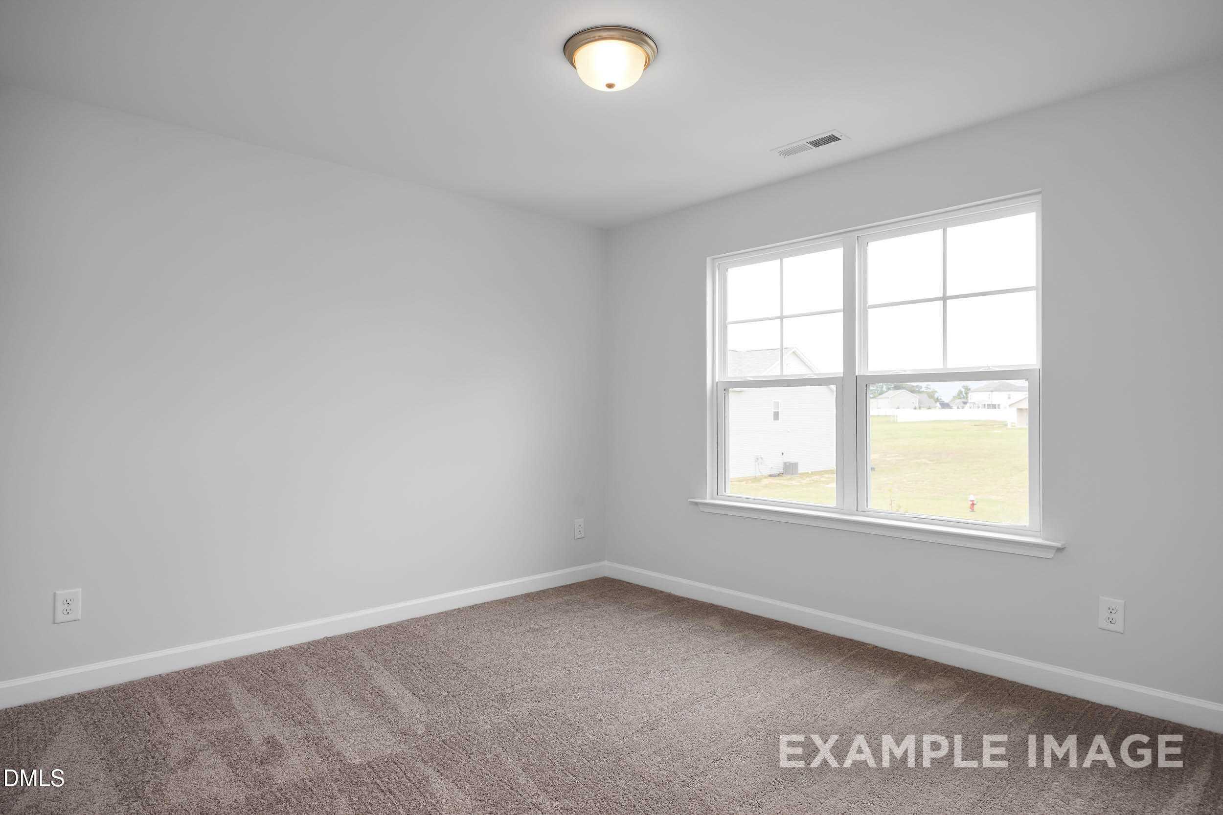 Bright bedroom with neutral gray walls, beige carpet, flush-mount ceiling light, and large windows in Davidson Homes The Ash B, Lillington, NC
