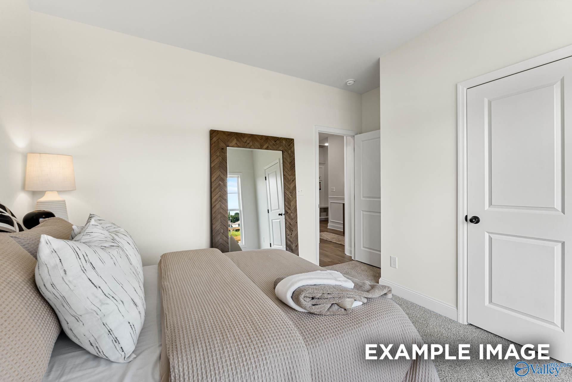 Elegant master bedroom with beige bedding, large framed mirror, and ensuite bath in Davidson Homes The Franklin, Huntsville AL
