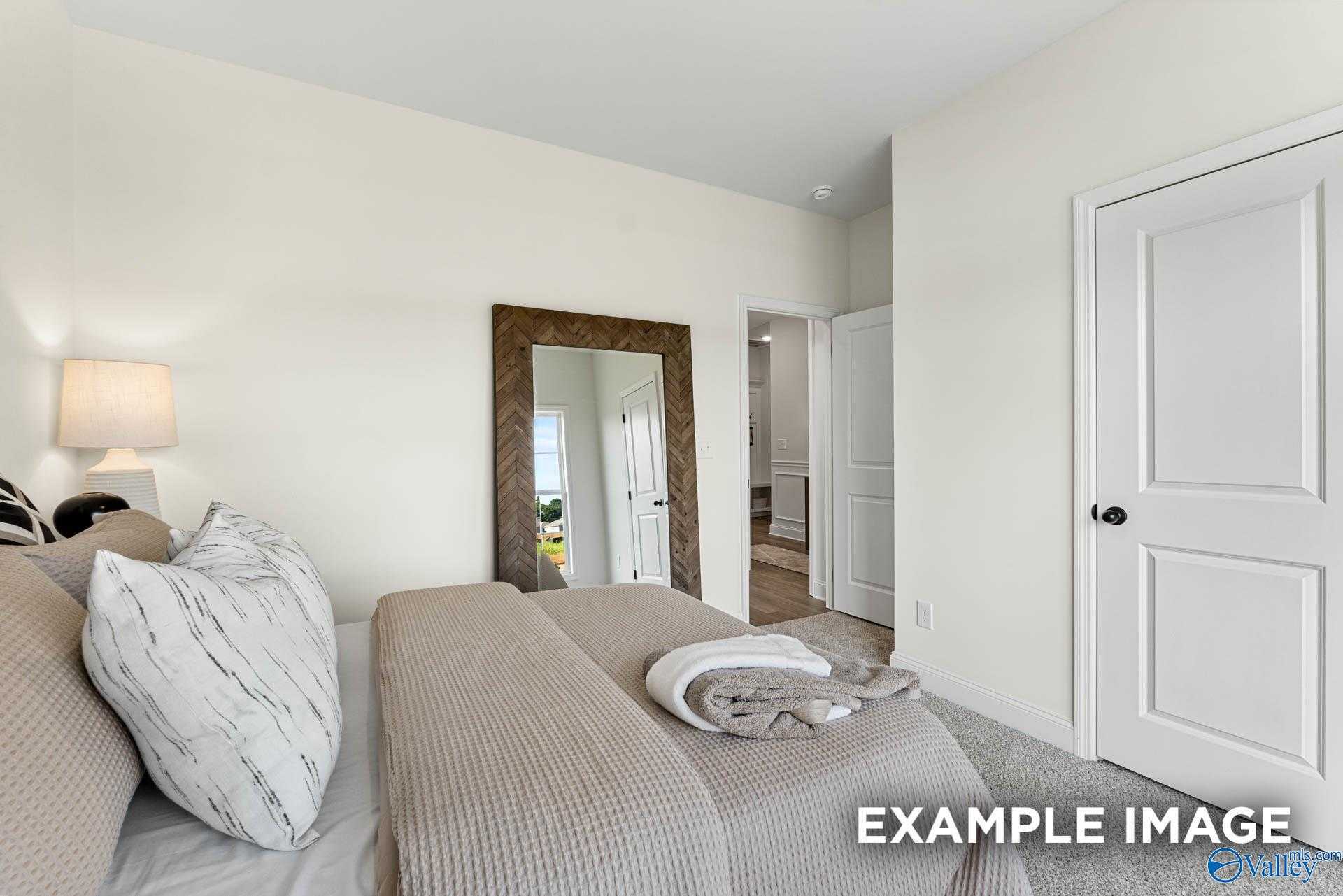 Serene master bedroom with neutral bedding, large framed mirror, and en-suite bath in Davidson Homes The Franklin, Huntsville