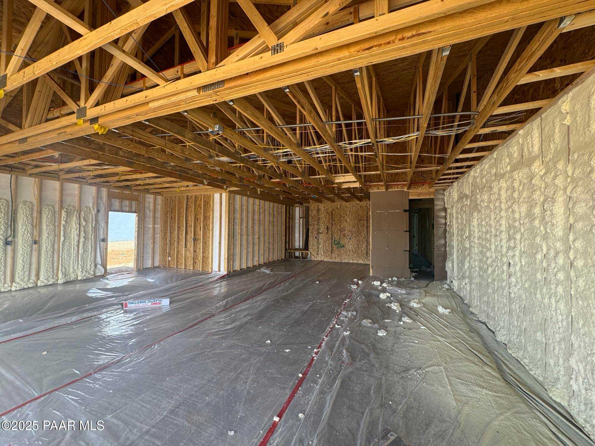 Unfinished spacious interior with exposed wooden trusses, insulated walls, and protective flooring in Evermore Homes The Sunrise A, Prescott Valley, Arizona