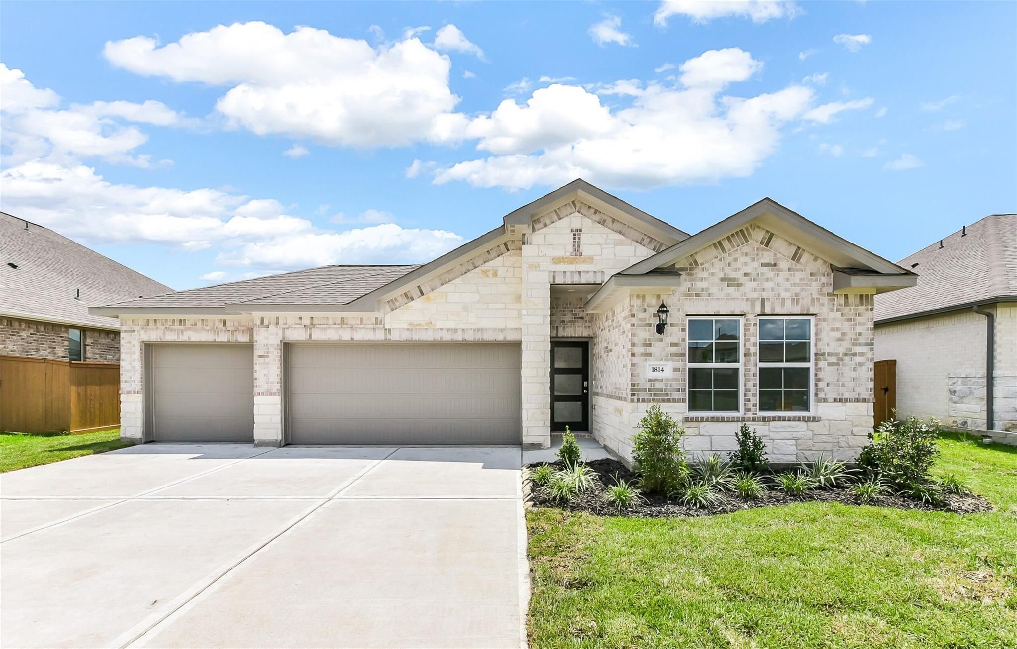 Modern 1-story beige brick home with 3-car garage, driveway, and lush landscaping in Sierra Vista, Rosharon, Texas