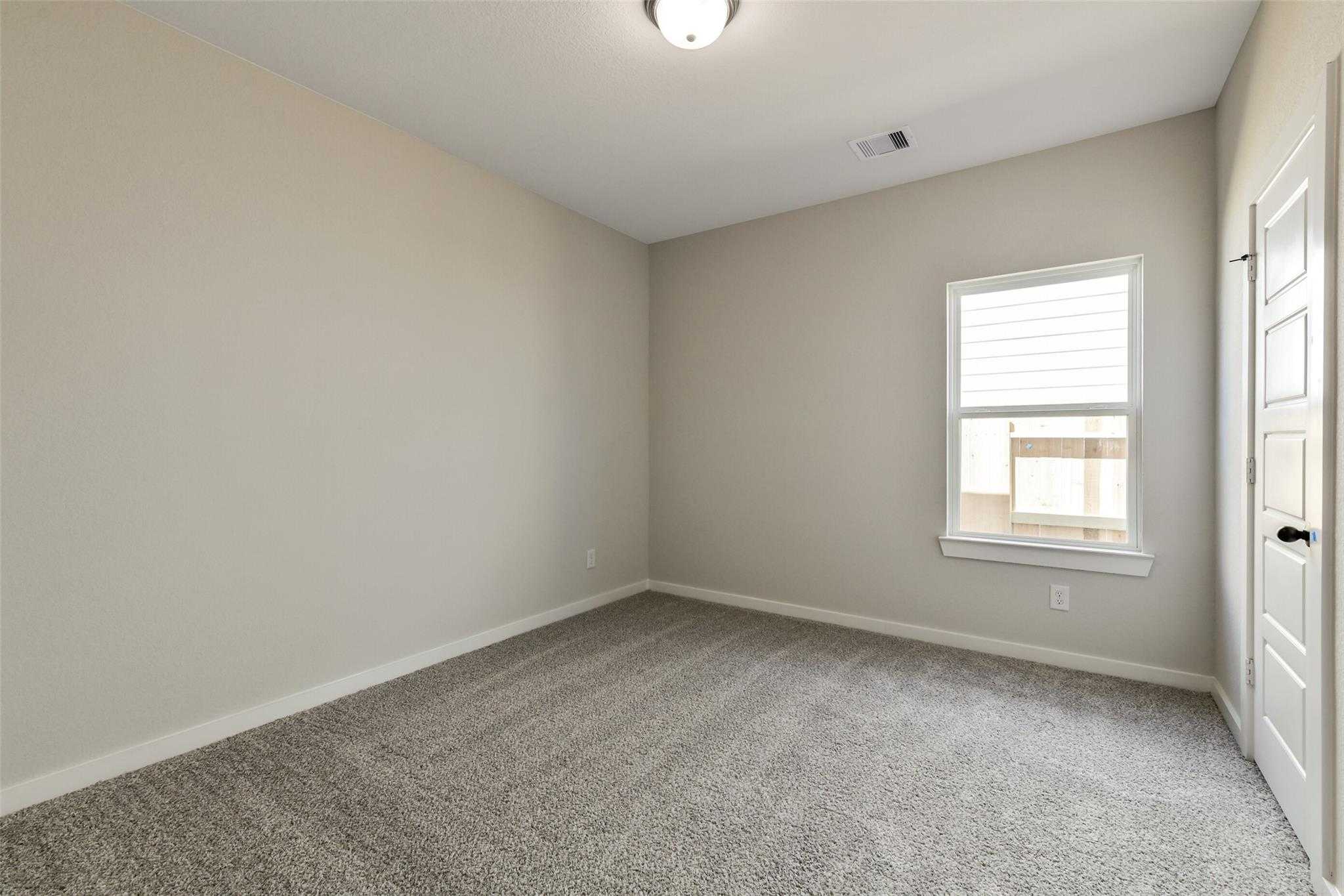 Cozy empty bedroom with beige walls, gray carpet, large window blinds, and interior door in Davidson Homes The Daphne H, Sundance Cove, Crosby, Texas