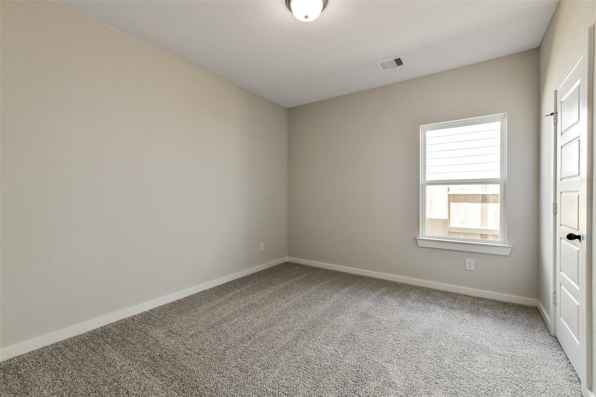 Cozy empty bedroom with beige walls, gray carpet, large window blinds, and interior door in Davidson Homes The Daphne H, Sundance Cove, Crosby, Texas
