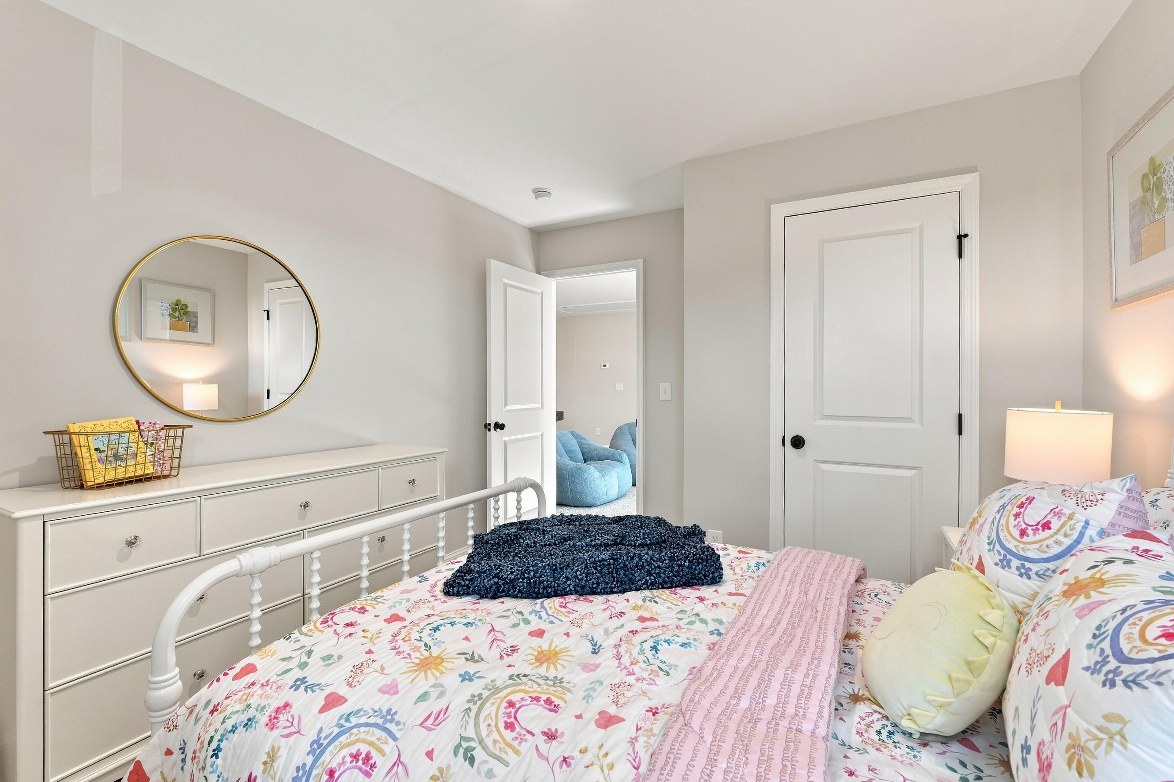 Bright bedroom at Bailey Park in Fayetteville, Tennessee by Davidson Homes with white metal bed, floral bedding, and dresser