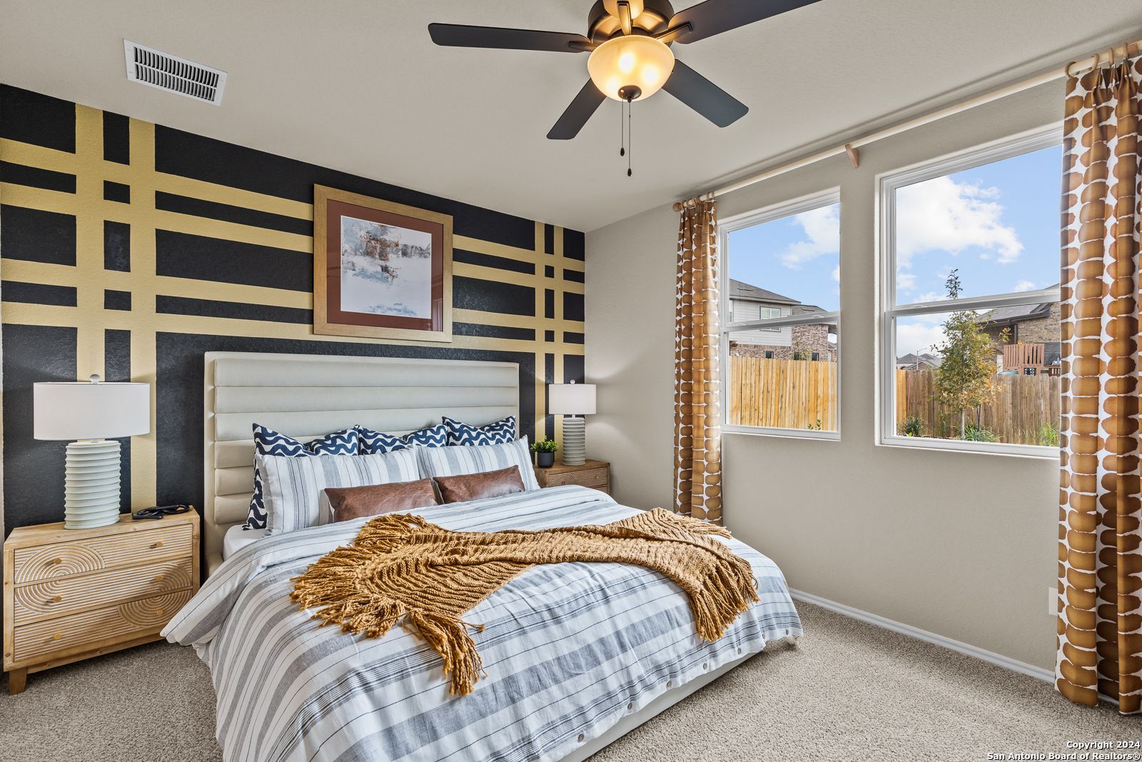 Cozy master bedroom with king bed, striped bedding, accent wall, ceiling fan, and backyard view in Davidson Homes The Douglas F, San Antonio
