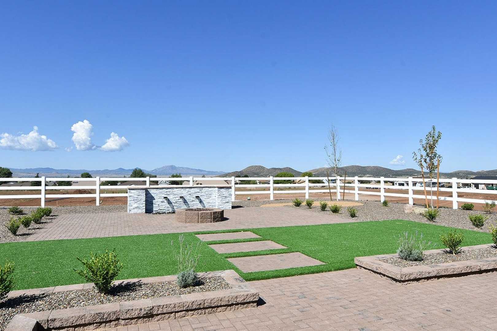 Spacious backyard of The Summit B with stone water feature, fire pit, paver paths, turf lawn, and Prescott Valley mountain views