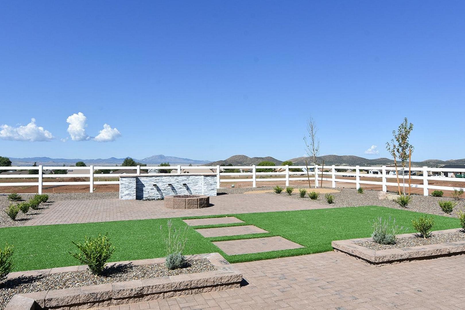 Spacious backyard of The Summit E featuring central fountain, white ranch fence, artificial turf, pavers, and Prescott Valley mountain views