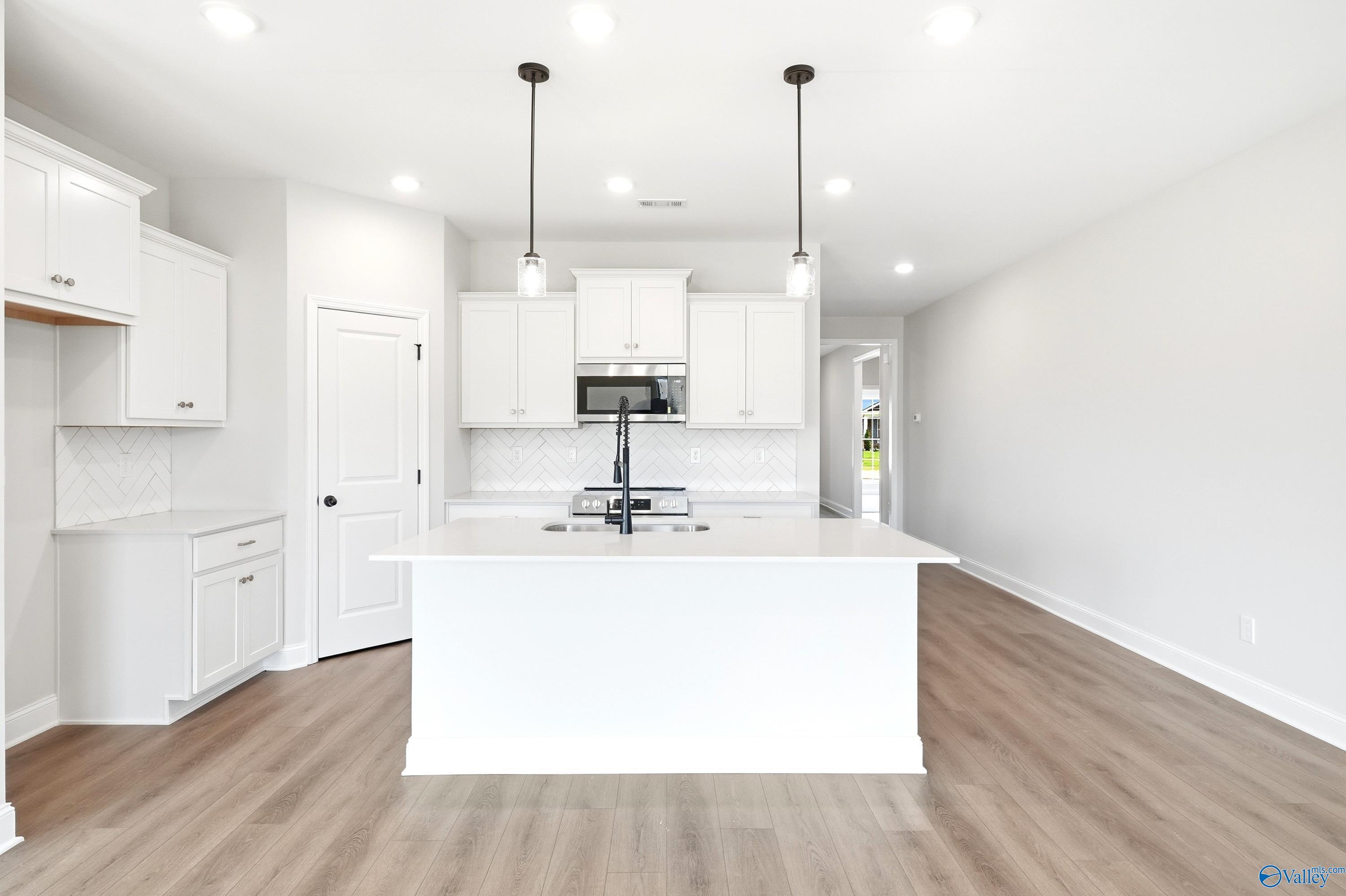 Modern white kitchen with island, pendant lights, and herringbone backsplash in The Daphne home at Lynn Meadows.