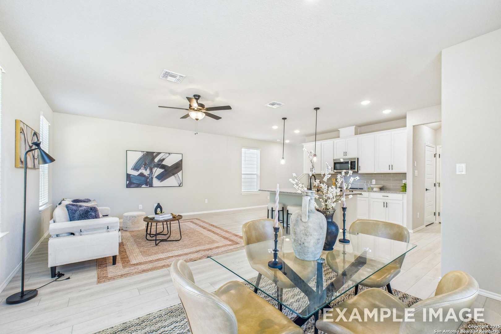 Open-concept living and dining area with white sofa, glass table, pendant lights, and modern kitchen in Davidson Homes The Charlotte A, San Antonio