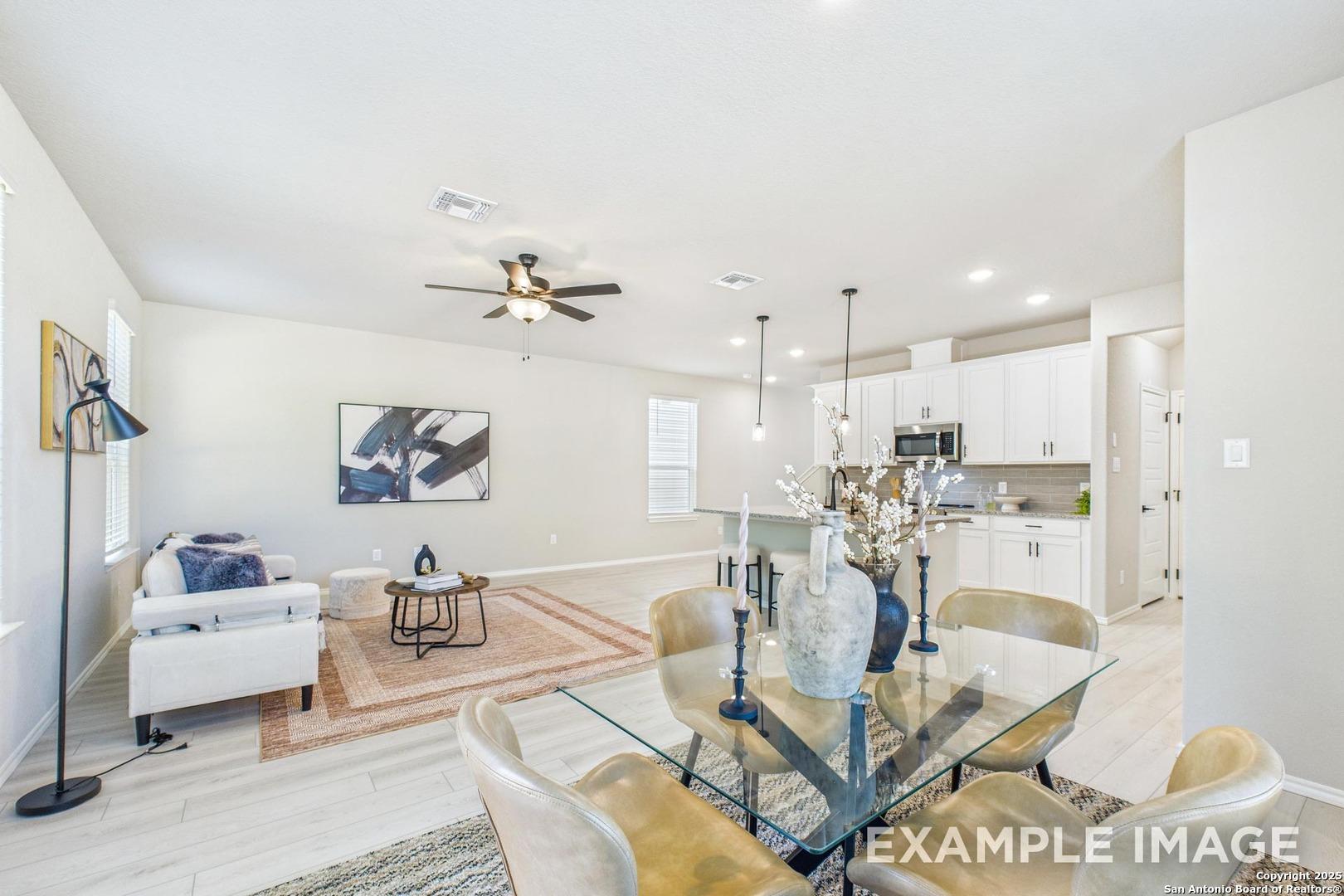 Open-concept living room with white sofa, glass dining table, ceiling fan, and adjacent kitchen in Davidson Homes The Charlotte B, San Antonio