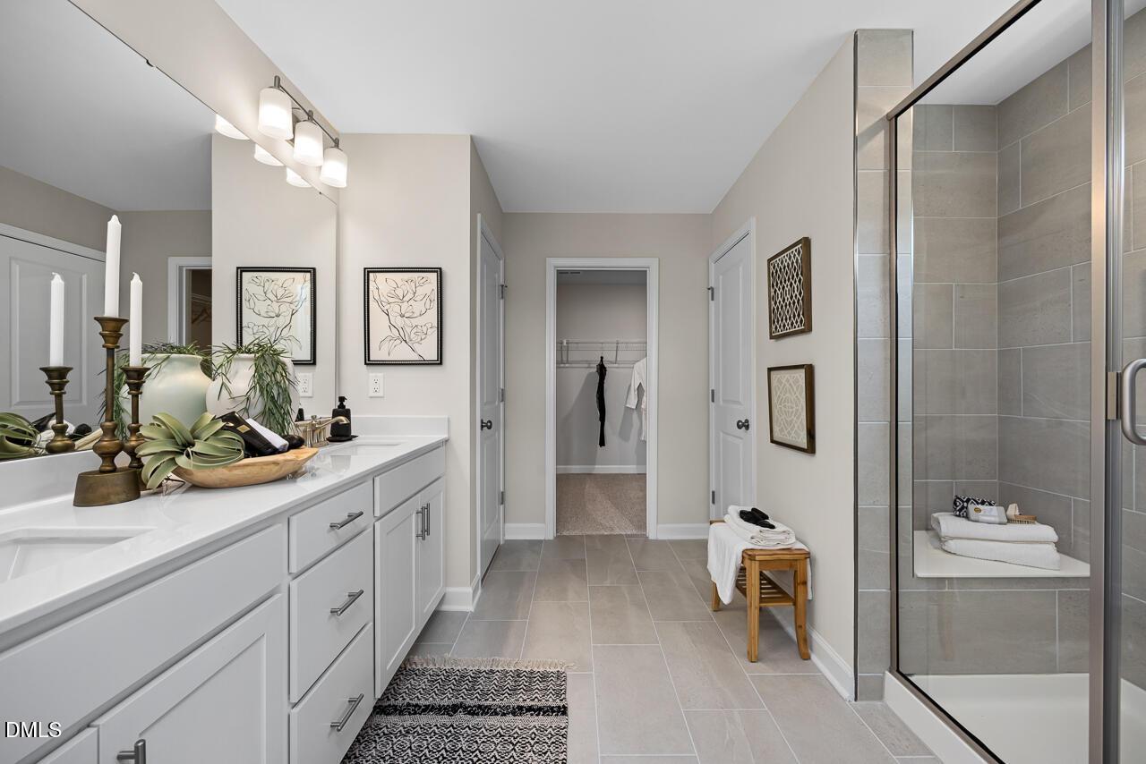 Modern master bathroom with double white vanity, glass shower, gray tile, and decor in Davidson Homes The Hickory II C, Zebulon, NC
