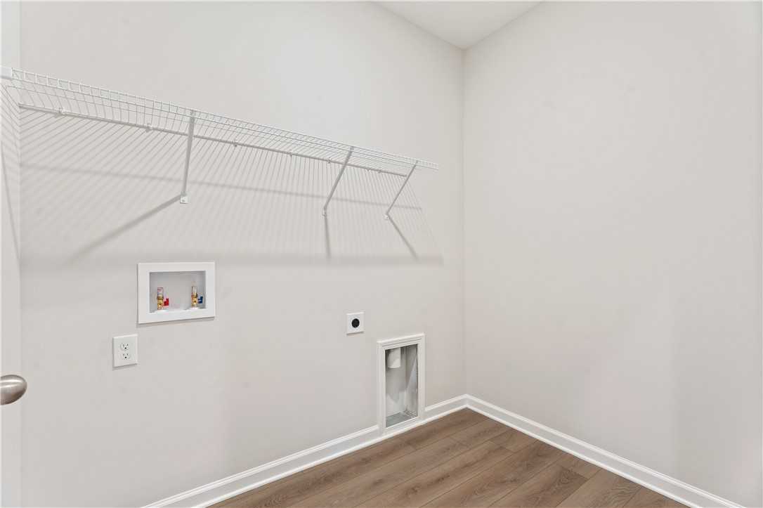 Clean laundry room featuring wire shelving, washer-dryer hookups, and utility sink in Davidson Homes The Luna B, Opelika, Alabama