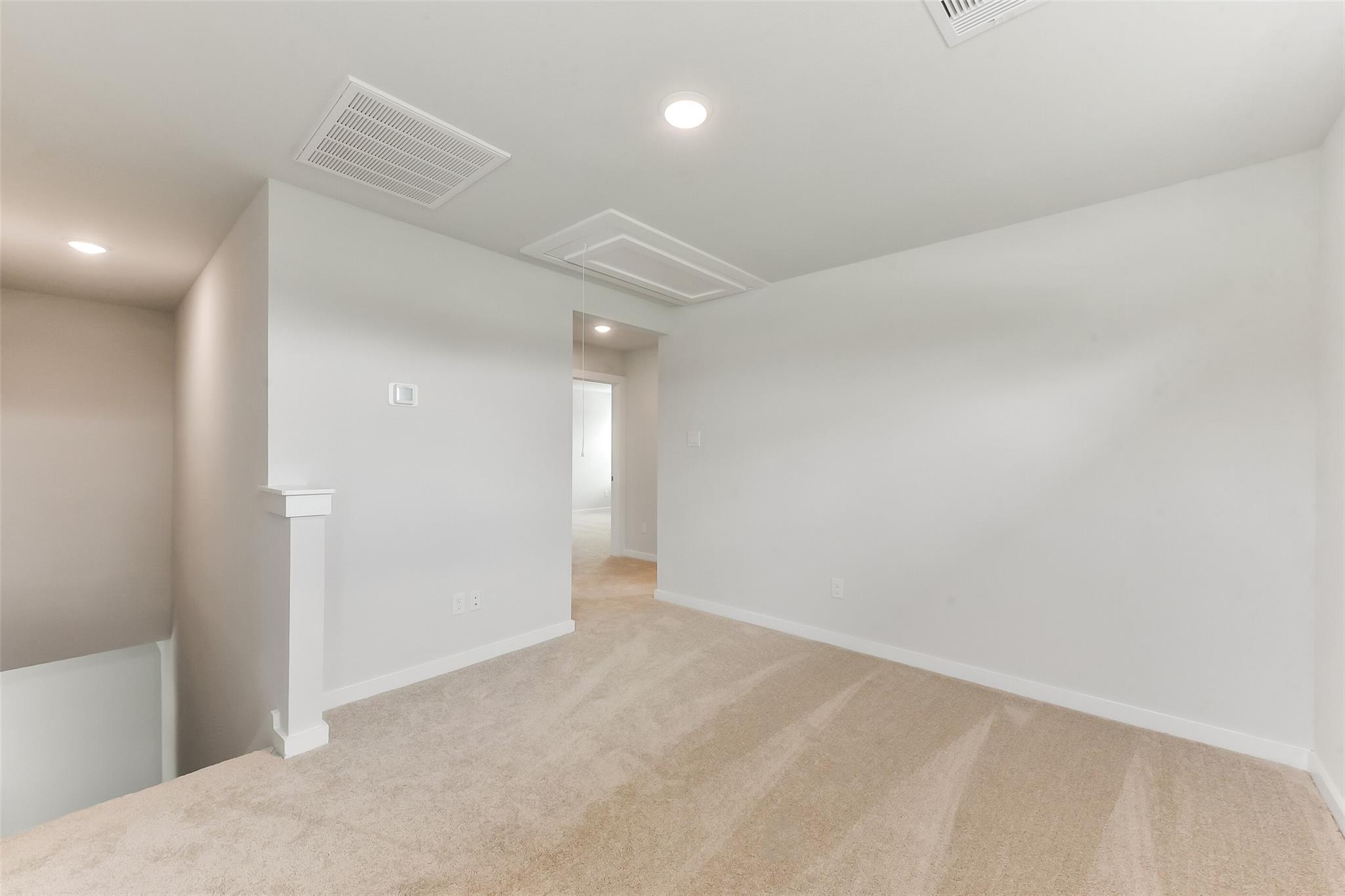Spacious upstairs hallway with beige carpet, white walls, railing overlooking stairs in Davidson Homes The Sabine F, Dayton, Texas