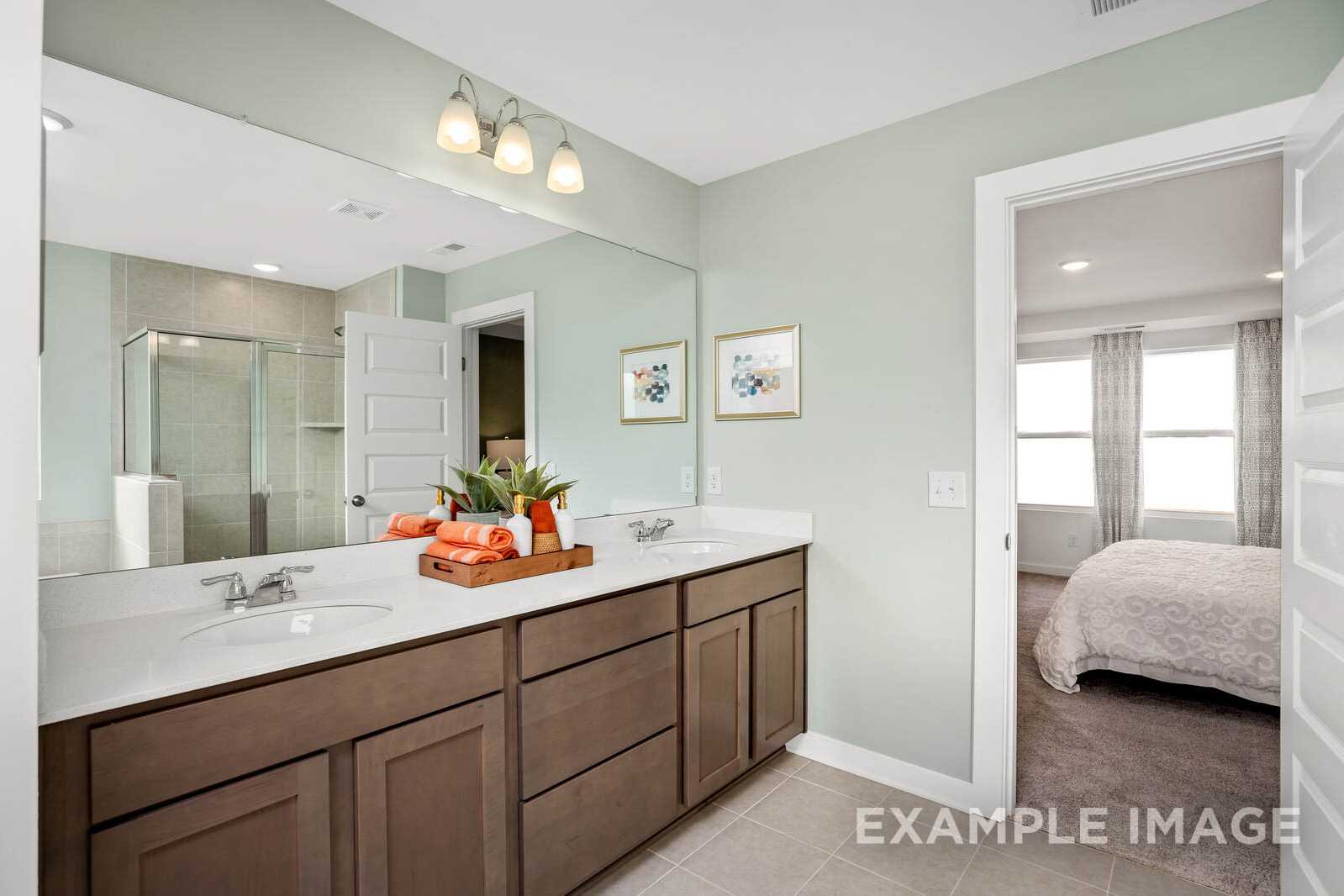 Spacious master bathroom in The Gordon B featuring dual wood vanity, large mirror, walk-in shower, and soft green walls