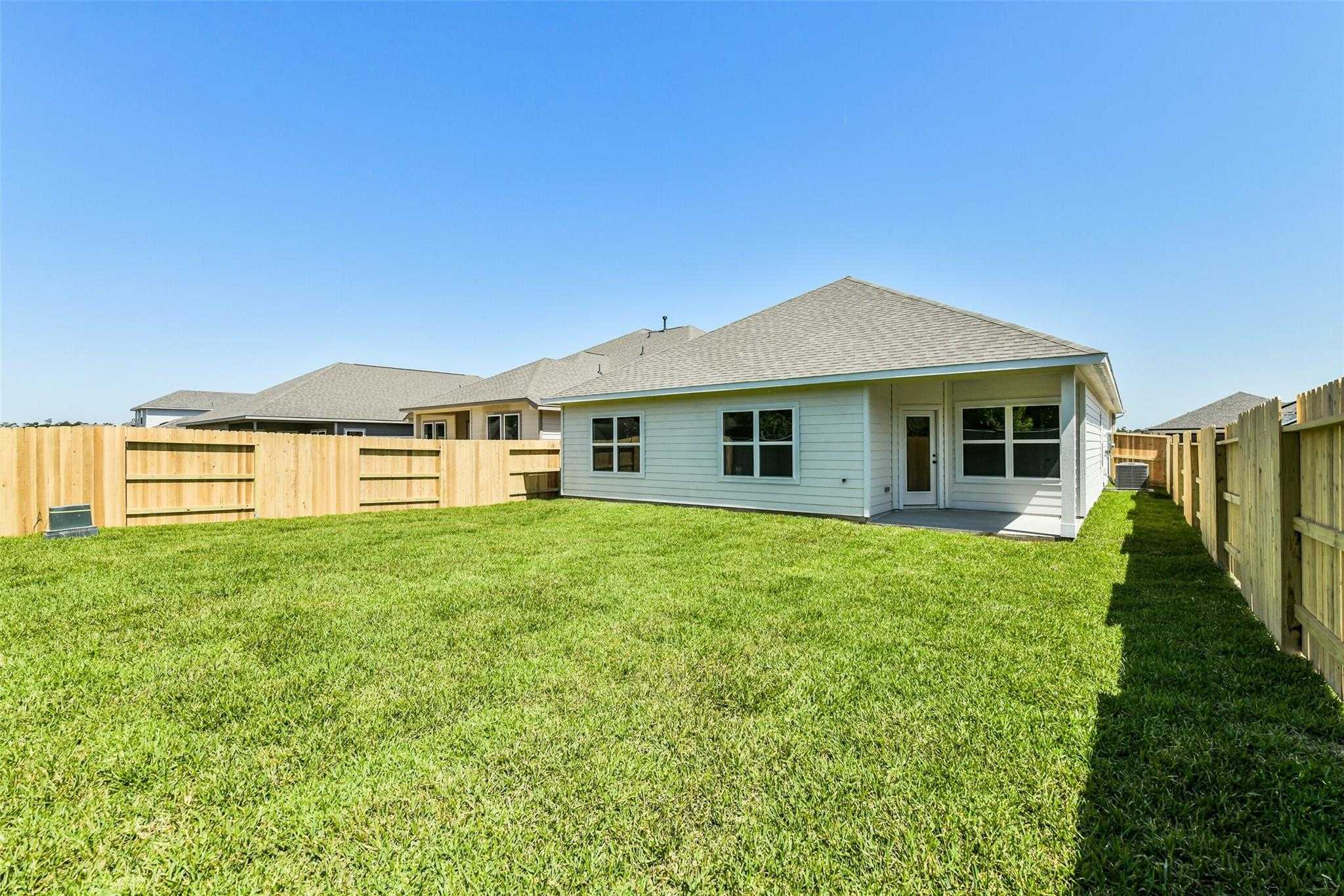 Lush green backyard with covered patio and white single-story home in Sundance Cove, Crosby, Texas - Davidson Homes The Daphne H
