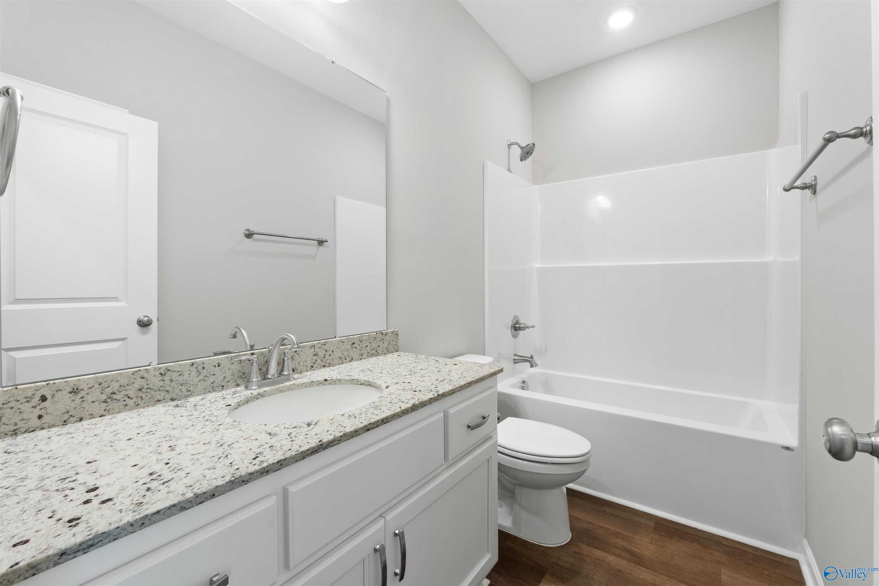 Bright bathroom with granite vanity, soaking tub, shower combo, and wood flooring in Davidson Homes The Luna, Hazel Green, Alabama