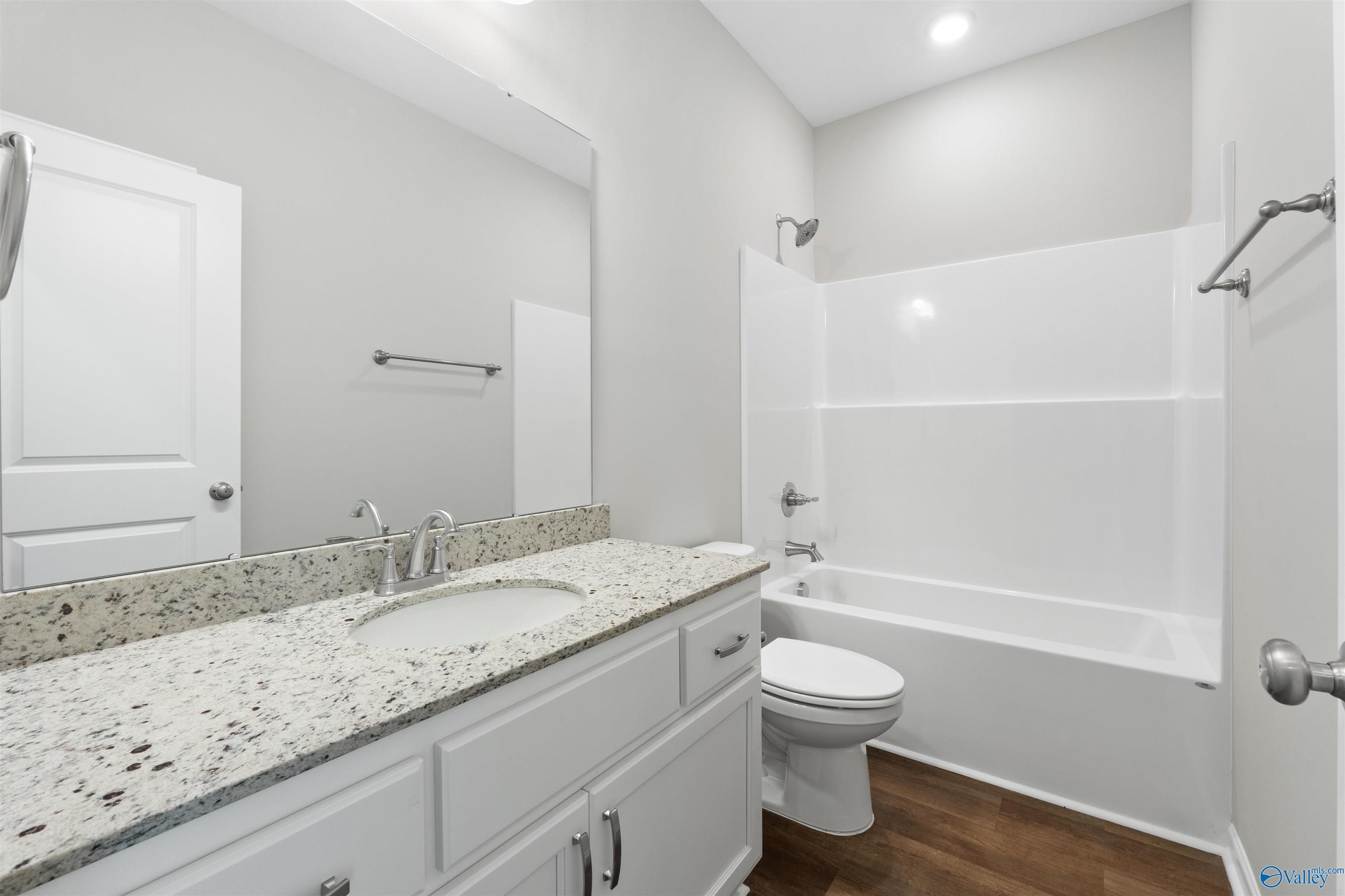 Bright bathroom with granite vanity, soaking tub, shower combo, and wood flooring in Davidson Homes The Luna, Hazel Green, Alabama