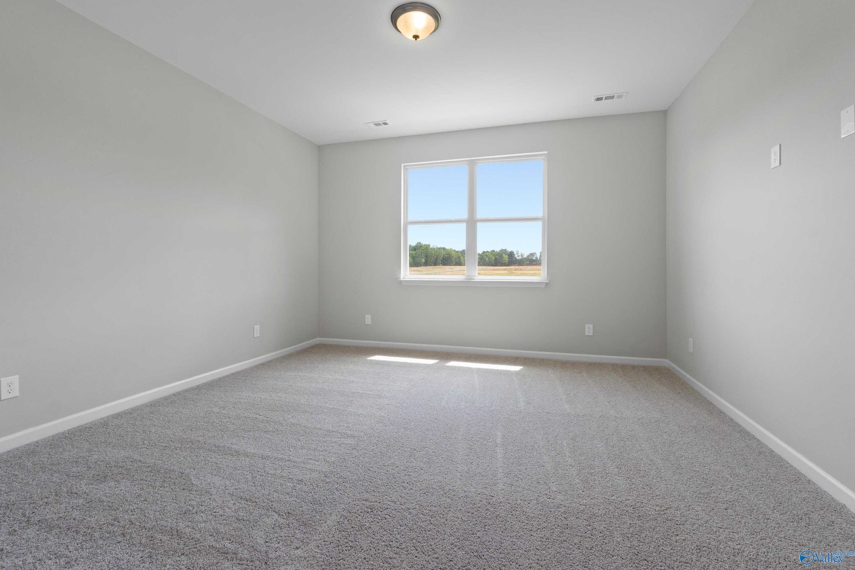 Bright secondary bedroom with light gray walls, large sunny window, and beige carpet in Evermore Homes The Aurora, Harvest, Alabama
