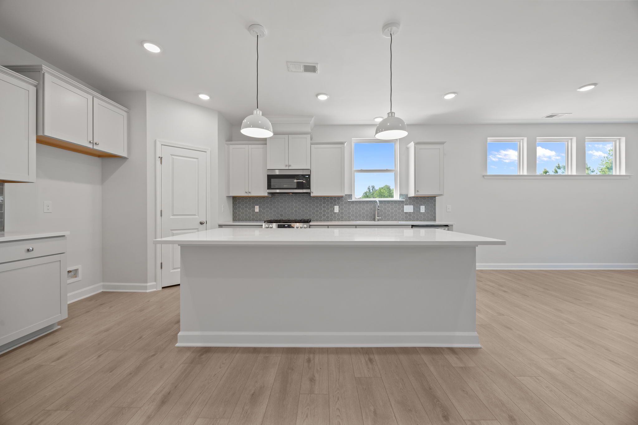 Modern kitchen in The Ashport B featuring a large center island, white cabinetry, and a grey honeycomb tile backsplash.