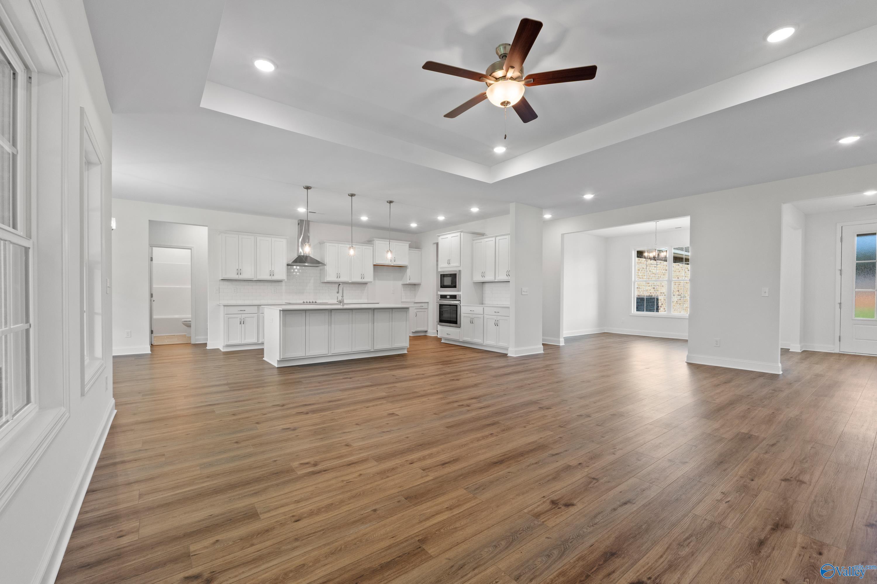 Open-concept kitchen-living area with white cabinets, central island, hardwood floors, ceiling fan in Davidson Homes The Oxford, Harvest, Alabama