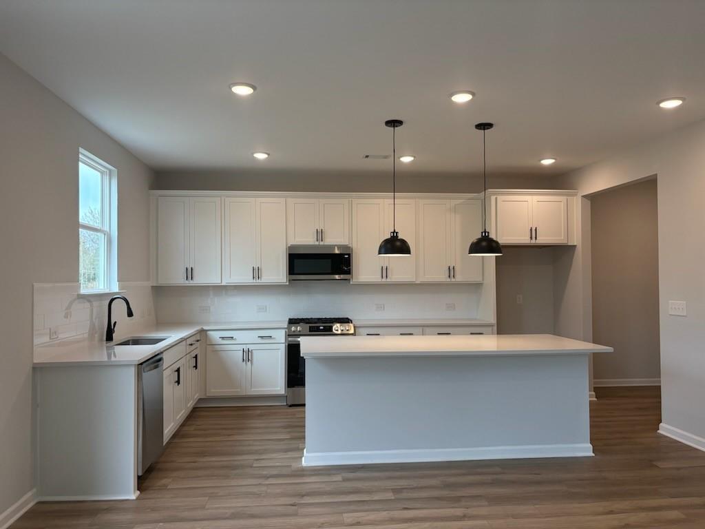 Modern white shaker kitchen with quartz island, stainless appliances, black pendants in Davidson Homes Hickory B, Winder GA