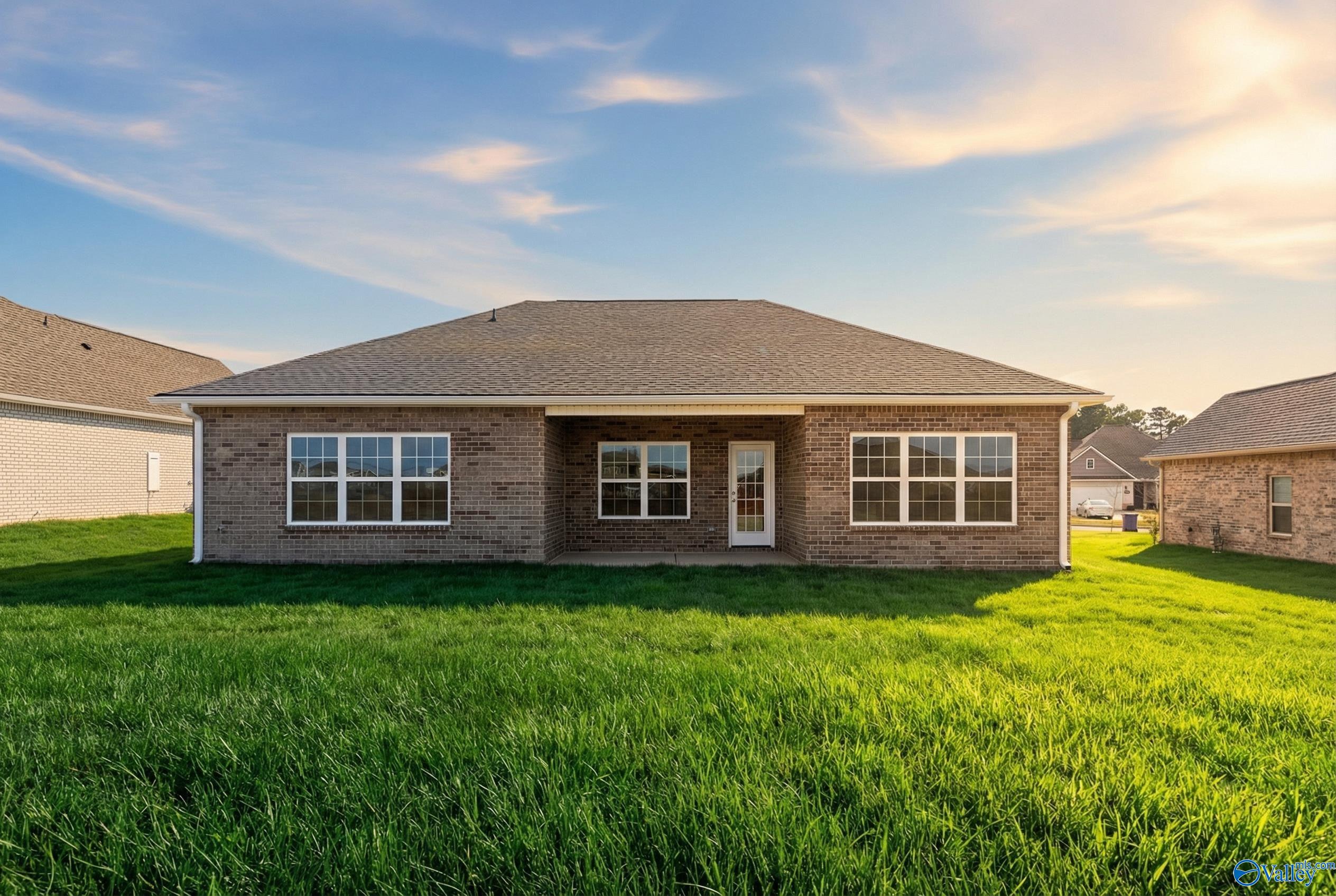 Rear view of brick single-story Montgomery C home with covered patio, large windows, lush green lawn, and sunset sky in Creekside, Harvest, Alabama