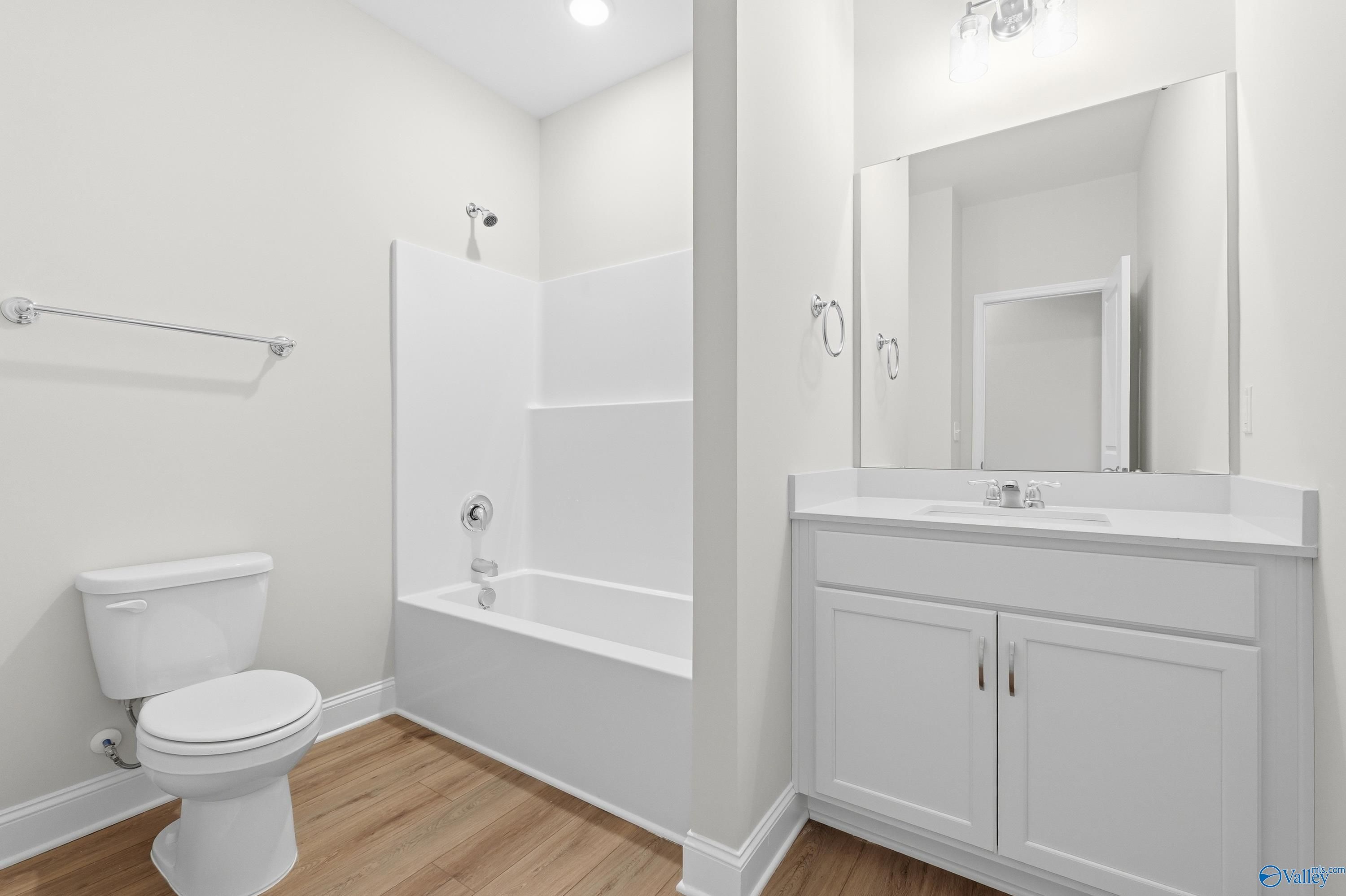 White bathroom with subway tile shower-tub combo, single vanity, mirror, and hardwood floors in Davidson Homes The Everett, Harvest AL