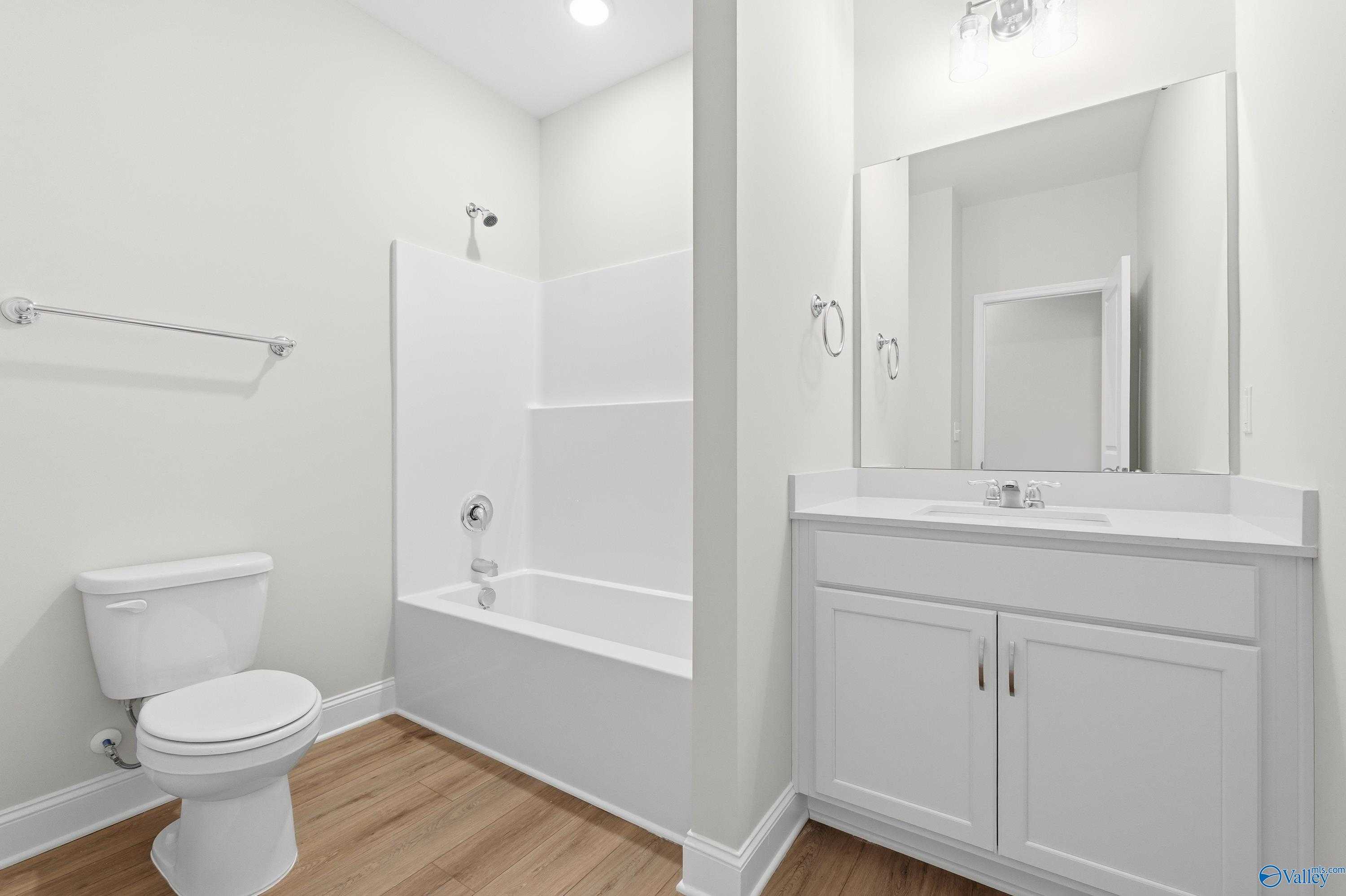 White bathroom with subway tile shower-tub combo, single vanity, mirror, and hardwood floors in Davidson Homes The Everett, Harvest AL