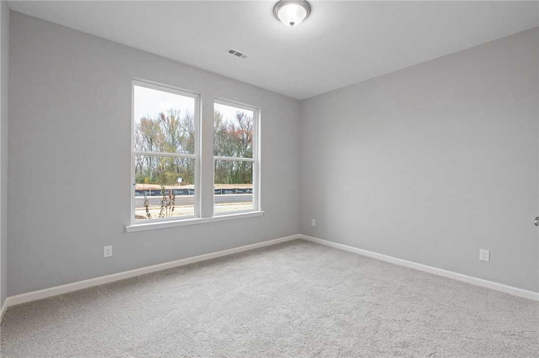 Bright secondary bedroom featuring light gray walls, plush carpet, and large windows with tree views in The Luna B, Opelika home
