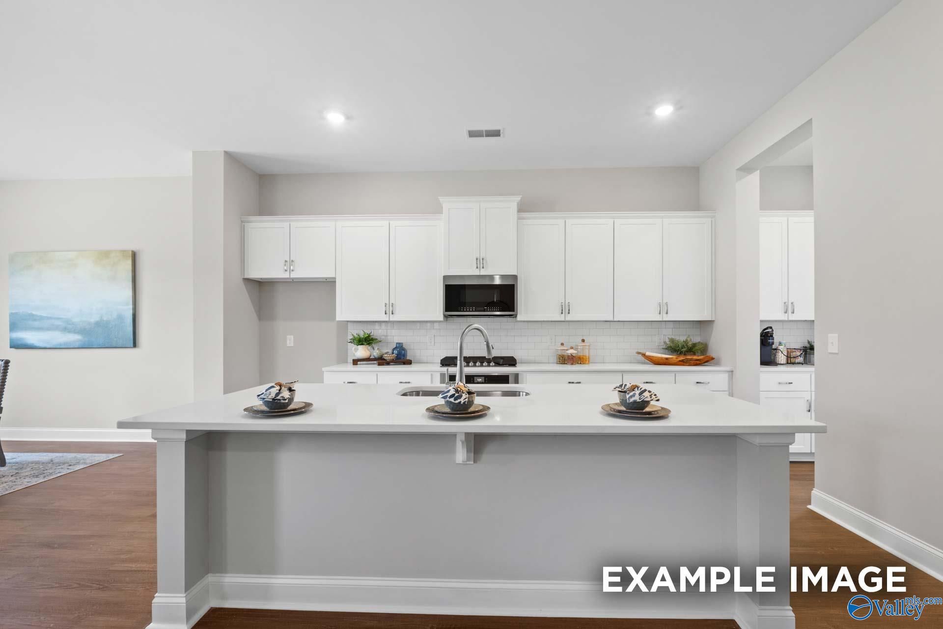 Elegant white shaker kitchen with oversized quartz island, stainless appliances, and subway tile in Evermore Homes The Haven E, Owens Cross Roads AL