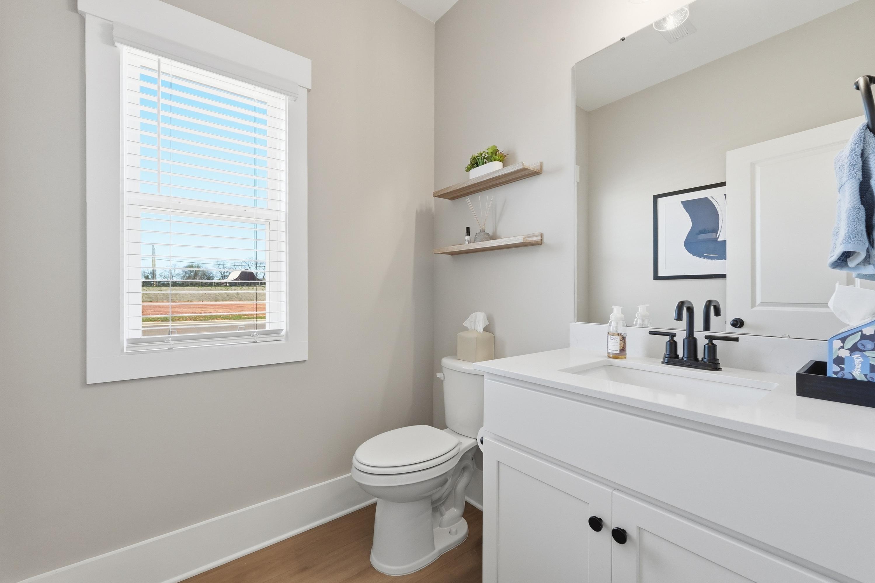 Modern powder room in Berry Cove, New Market Alabama featuring beige walls, white vanity sink, toilet, floating shelves and window blinds