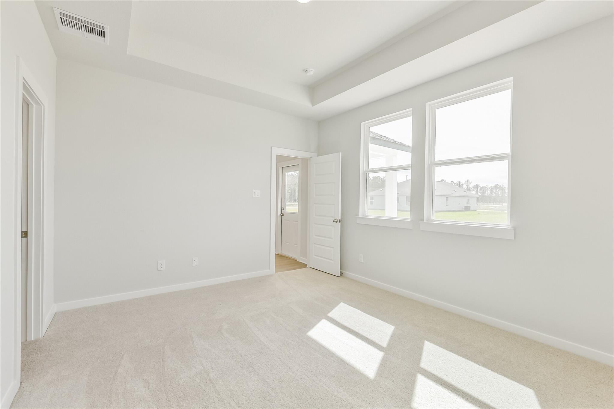 Bright bedroom with tray ceiling, beige carpet, and French door patio access in Davidson Homes The Frio G, Conroe, Texas