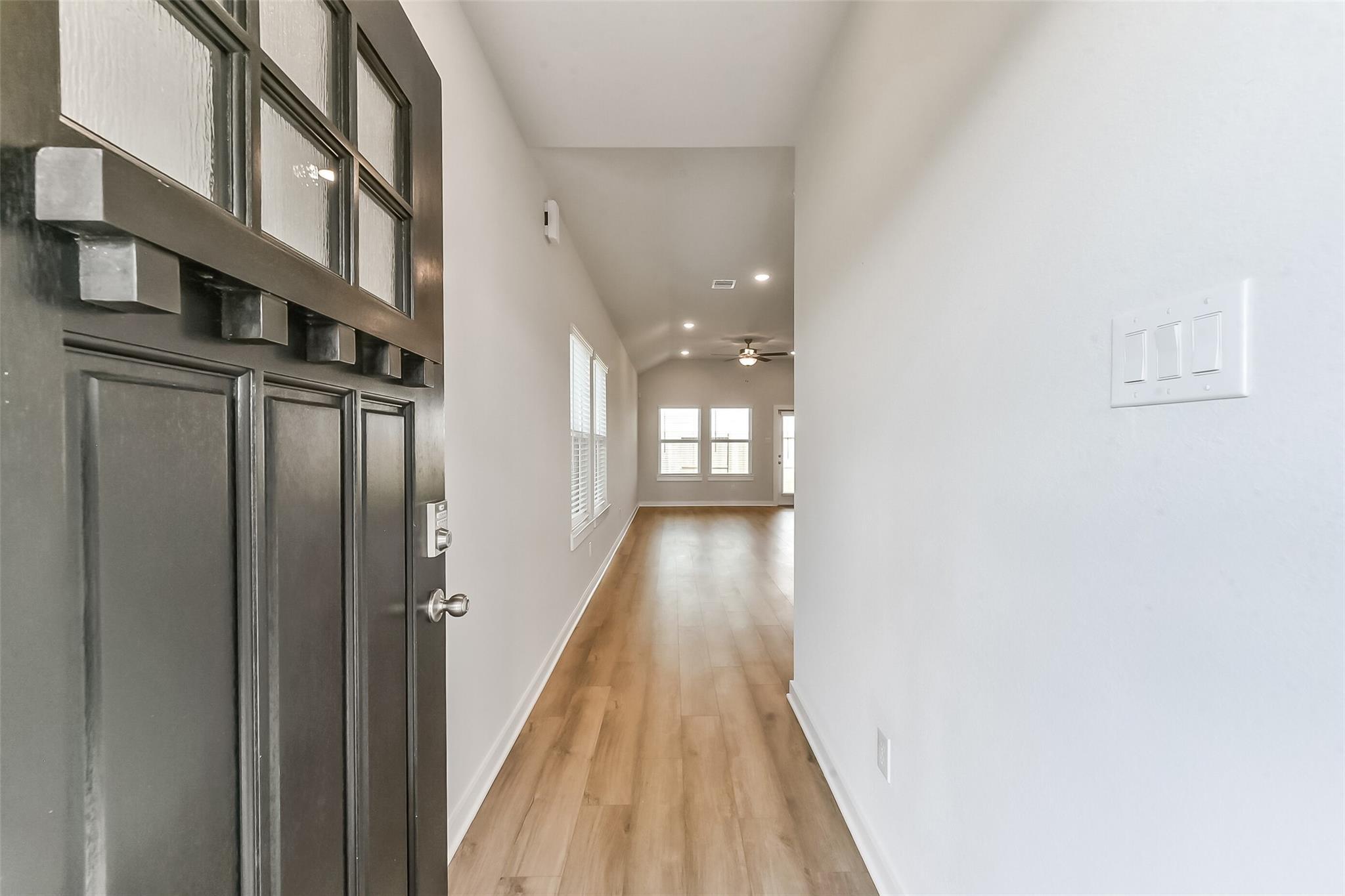 Welcoming entry hallway with dark wood door, frosted glass panels, oak floors and recessed lights in The Costa C home, Dayton, Texas