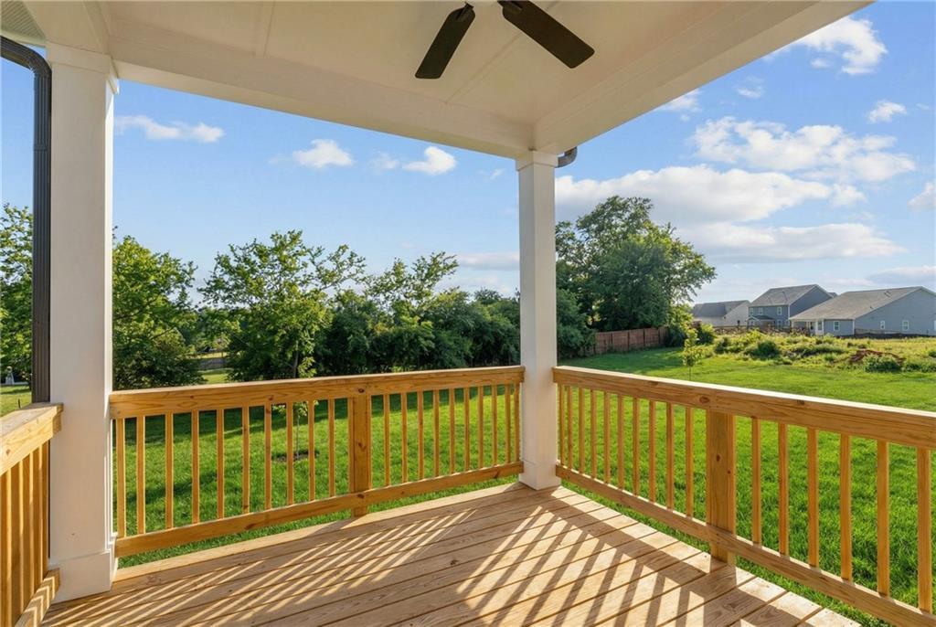 Covered wooden deck with white columns and ceiling fan overlooking lush green backyard in Davidson Homes The Willow B, Hoschton, Georgia