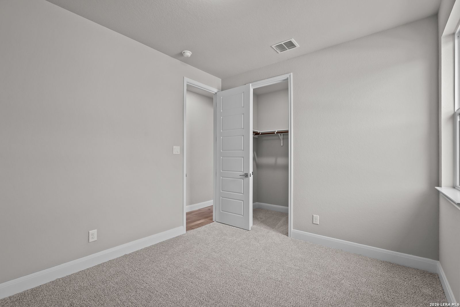 Spacious secondary bedroom with neutral gray walls, plush carpet, open closet, and window in Davidson Homes The Rockford G, Ladera, San Antonio