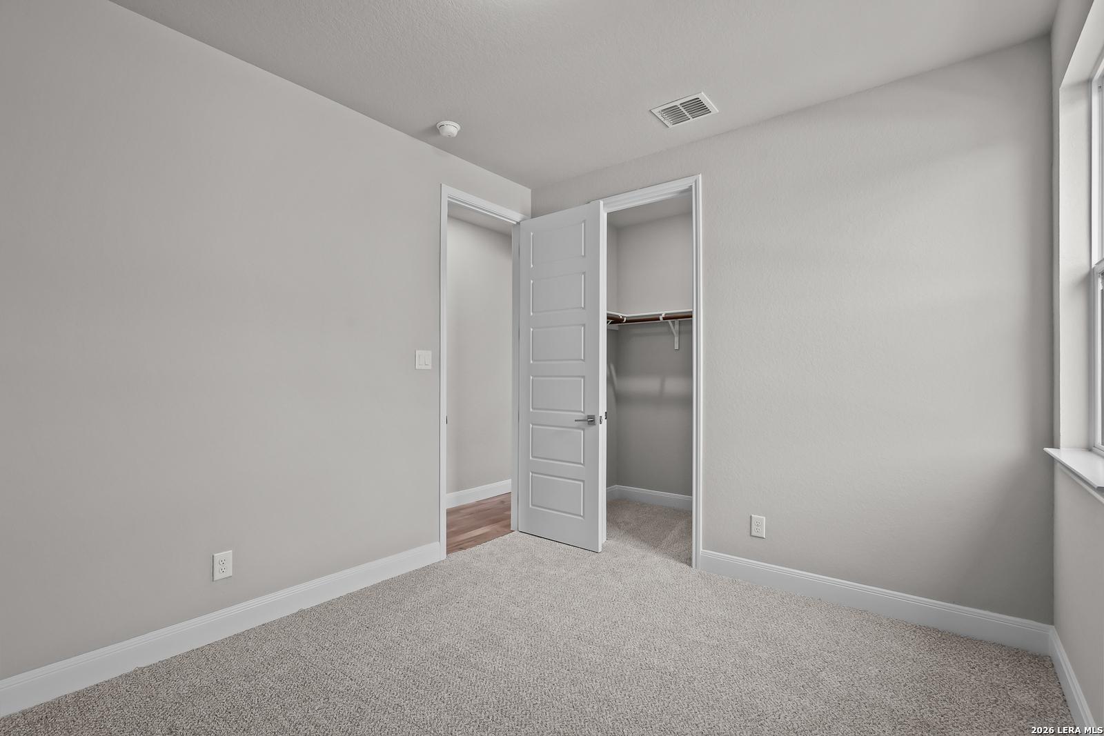 Spacious secondary bedroom with neutral gray walls, plush carpet, open closet, and window in Davidson Homes The Rockford G, Ladera, San Antonio