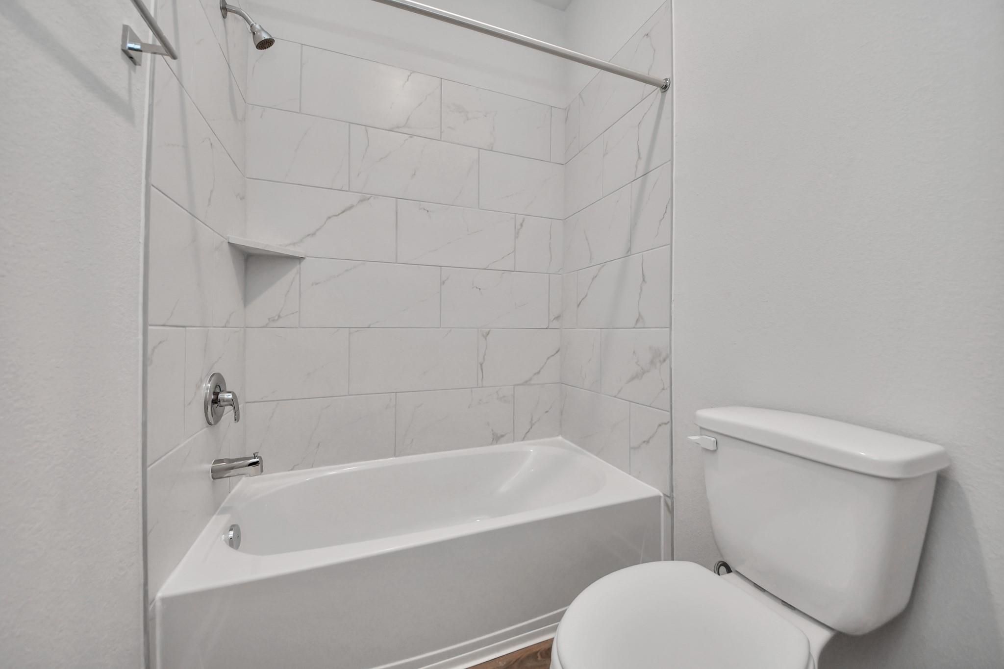 Modern bathroom with white marble-style tiled bathtub and shower in The Colorado G floor plan at Emberly, Beasley, Texas.