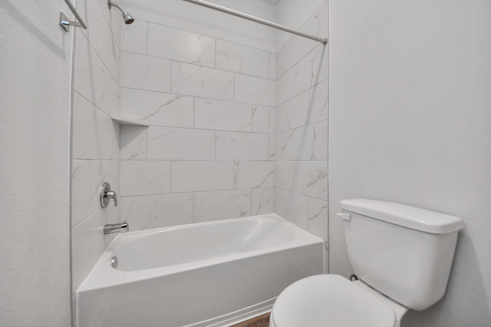 Modern bathroom with white marble-style tiled bathtub and shower in The Colorado G floor plan at Emberly, Beasley, Texas.