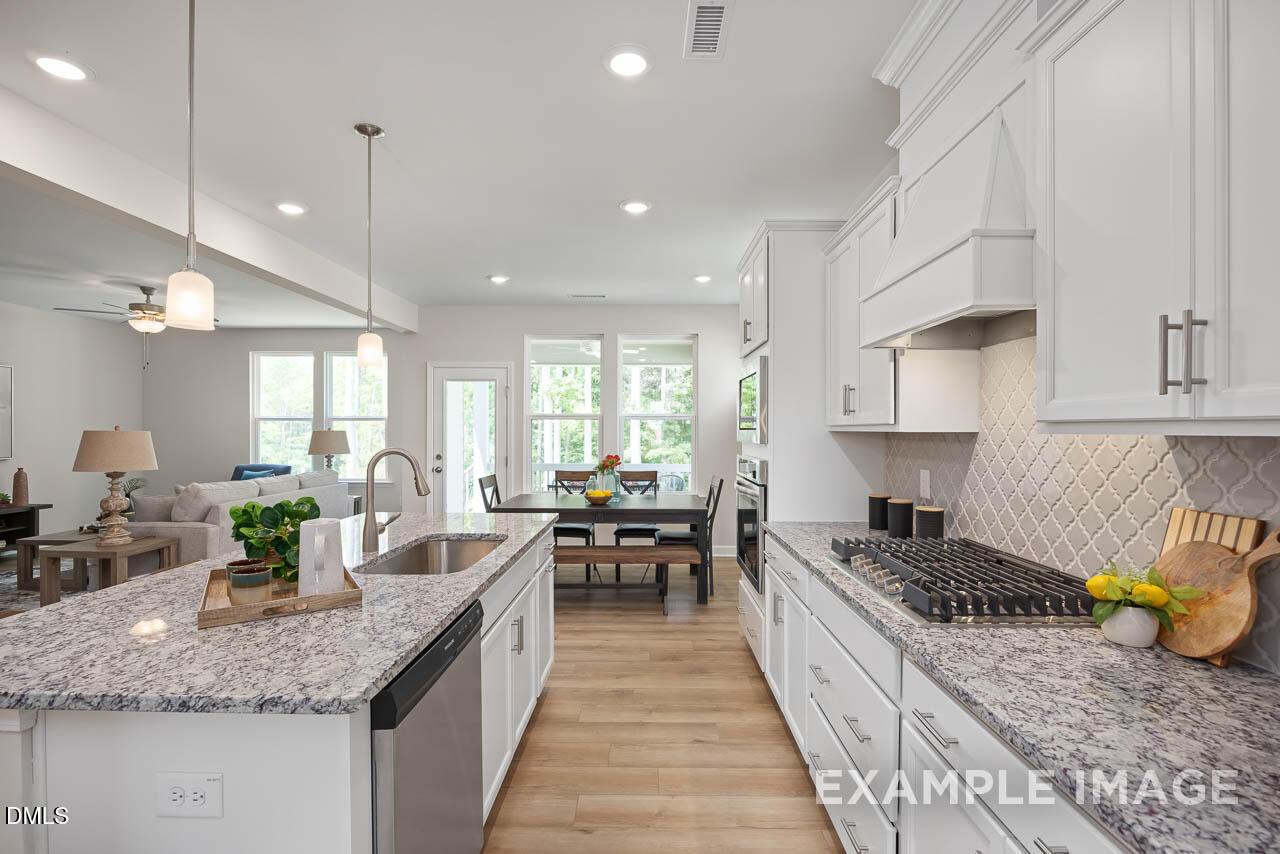 Modern open-concept kitchen with white cabinets, granite island sink, stainless appliances, and adjacent dining in The Willow D, Lillington, NC