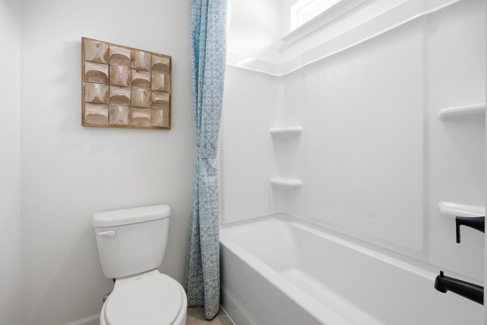 Modern full bathroom in The Ashport featuring a white tub-shower combo, sleek toilet, and decorative wall art.