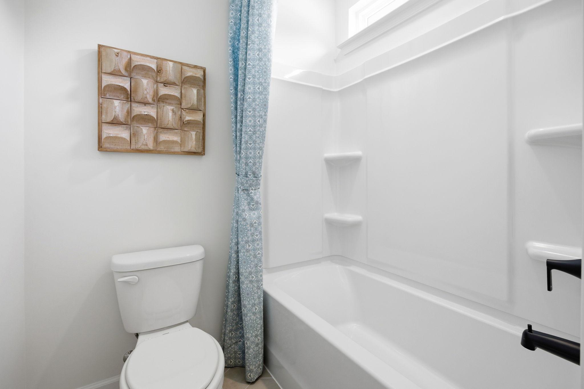 Modern bathroom in The Ashport K featuring a white tub-shower combo, toilet, and geometric wood wall decor.