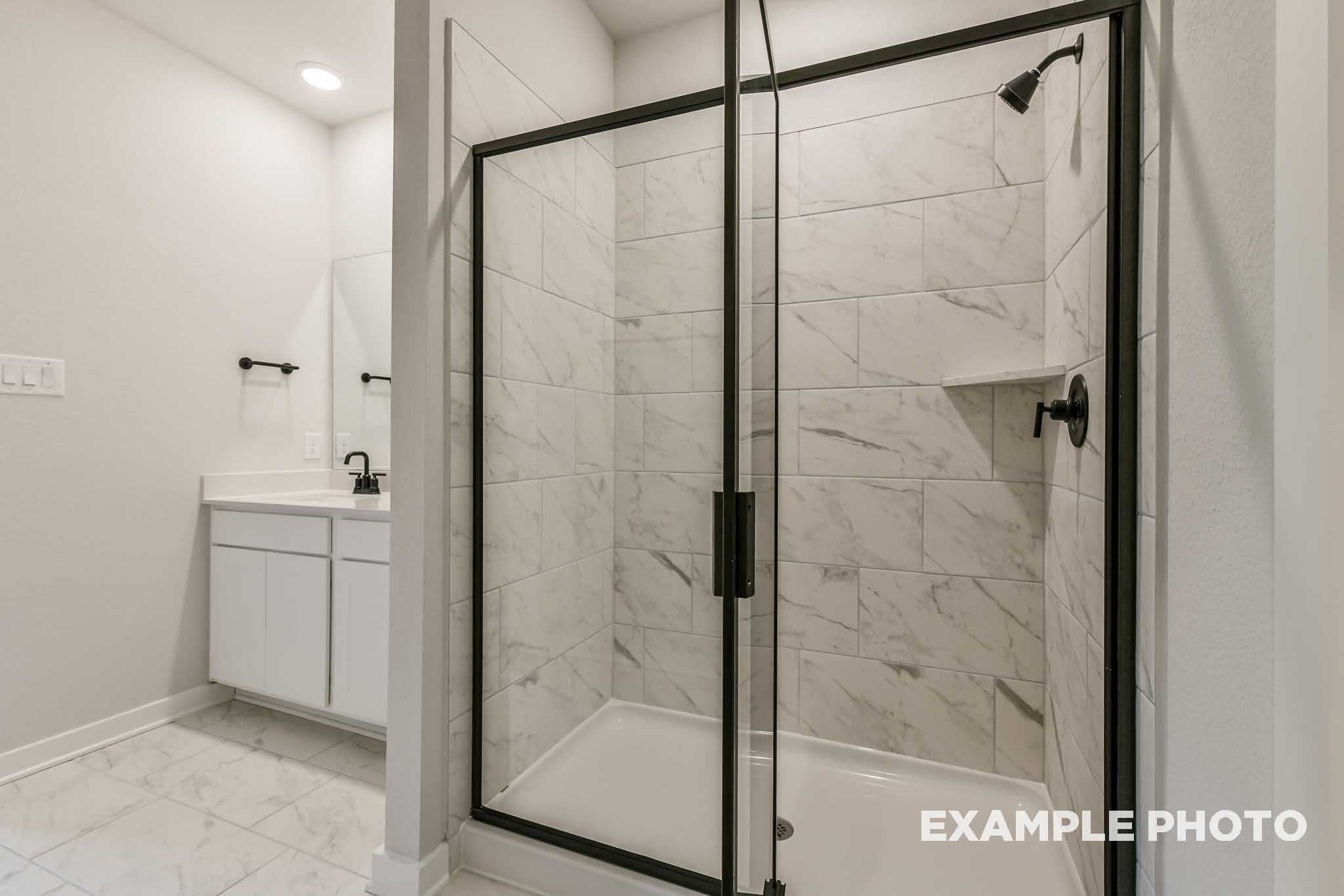 Spacious master bathroom in The Daphne G featuring frameless glass shower, white subway tile walls, and modern vanity